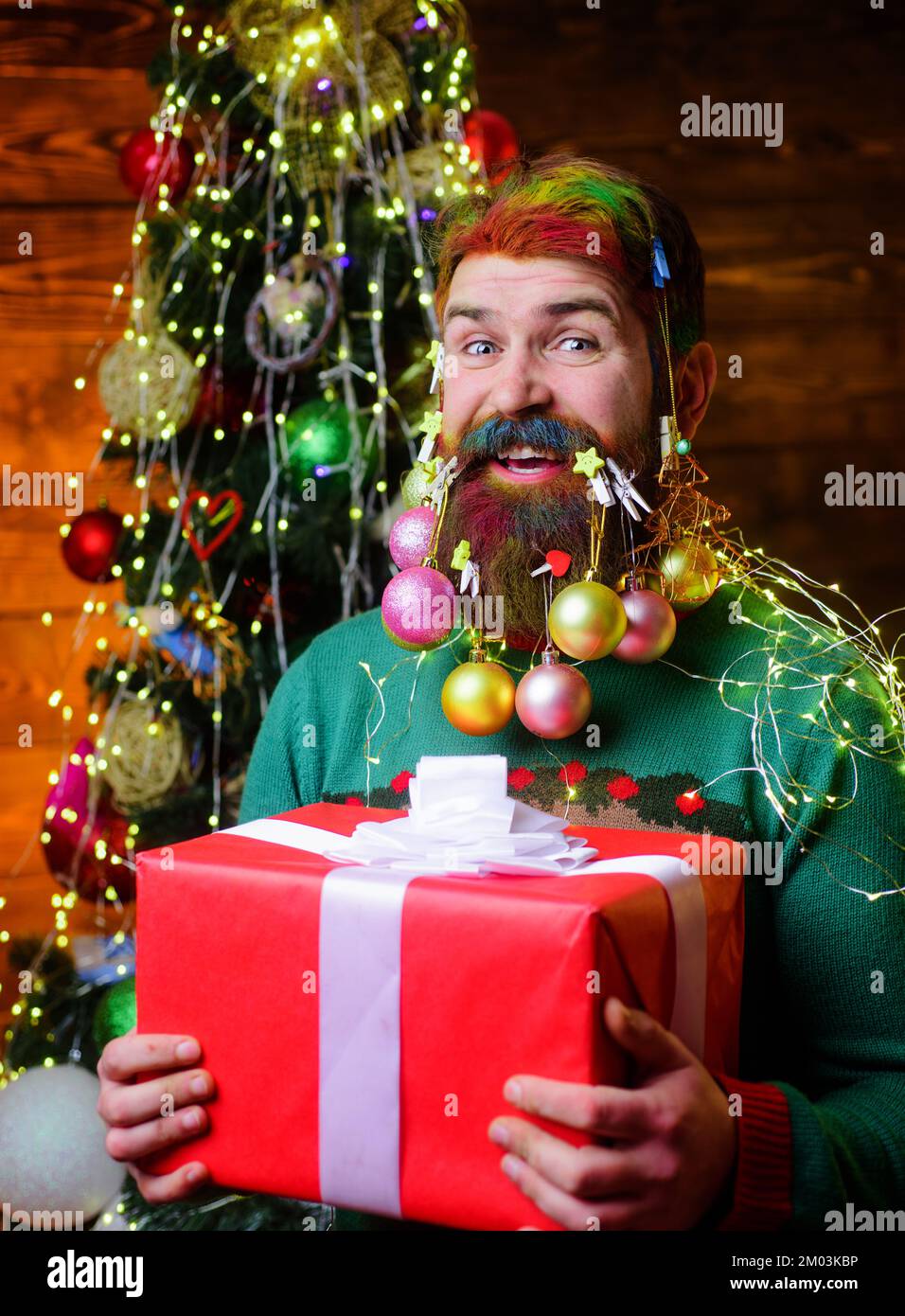 Merry Christmas and happy new year. Smiling man with decorated beard holds gift box. Winter holiday. Stock Photo