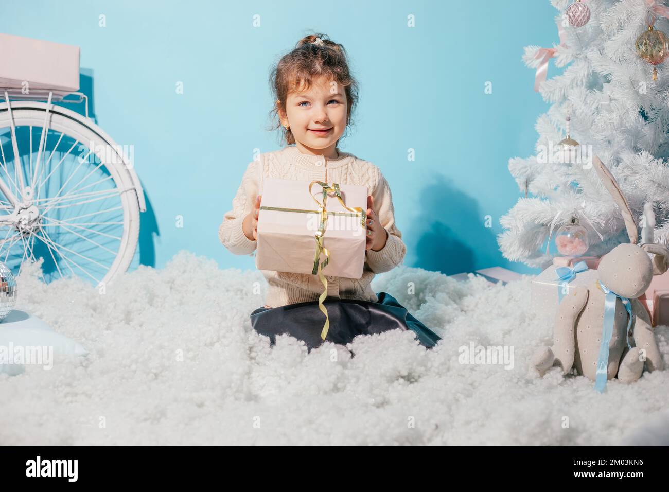 Smiling merry, positive little girl getting surprise present box, sitting on soft cozy wadding carpet like cloud against Stock Photo