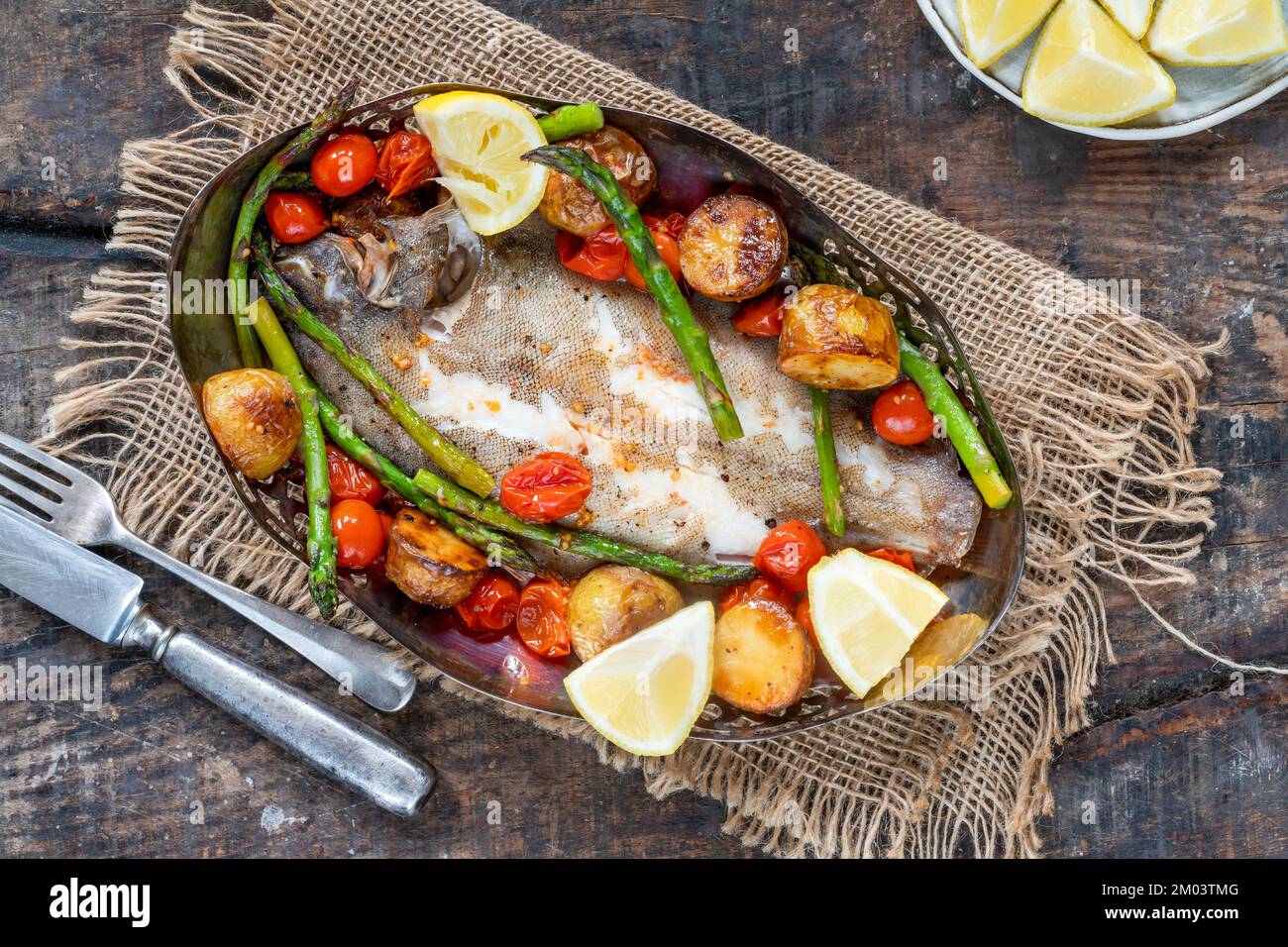 Lemon sole baked with potatoes, baby tomatoes and asparagus Stock Photo