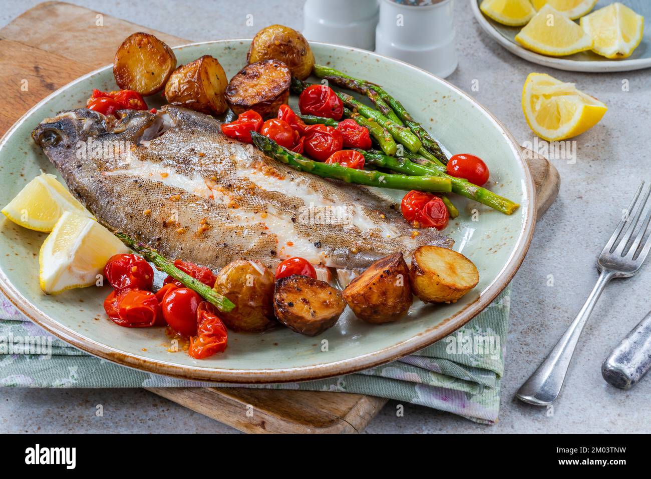 Lemon sole baked with potatoes, baby tomatoes and asparagus Stock Photo