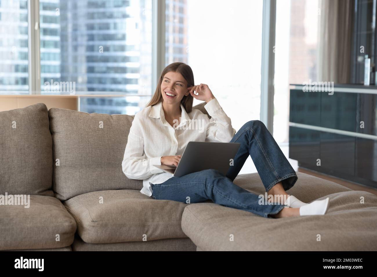 Cheerful beautiful young freelancer woman resting on soft comfortable sofa Stock Photo
