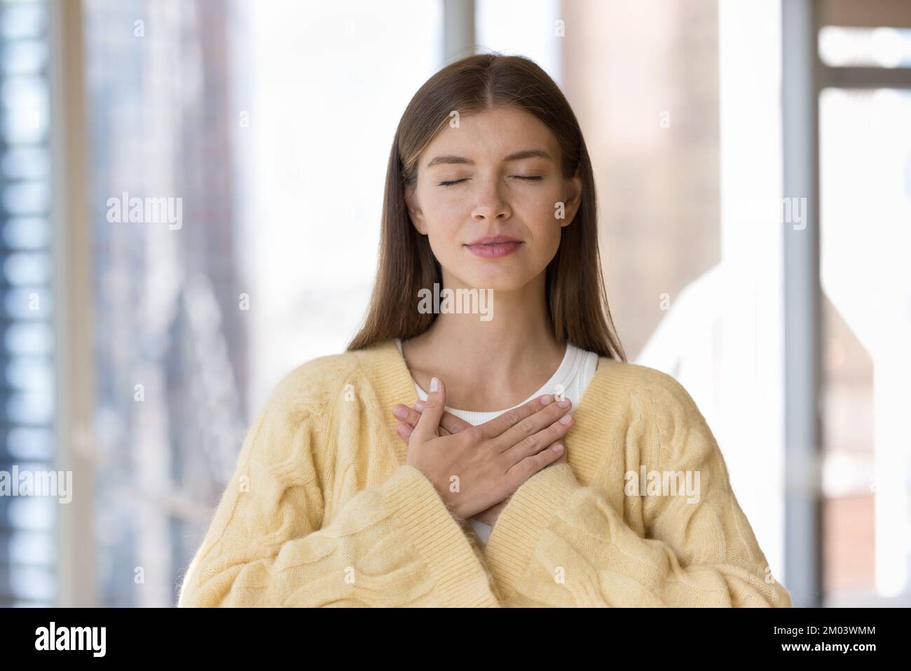 Peaceful beautiful young adult girl stacking hands on chest Stock Photo