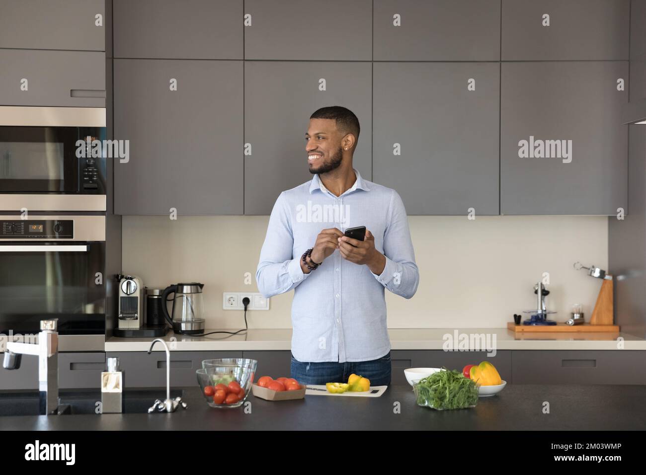 Joyful attractive young Black chef man holding smartphone, looking away Stock Photo