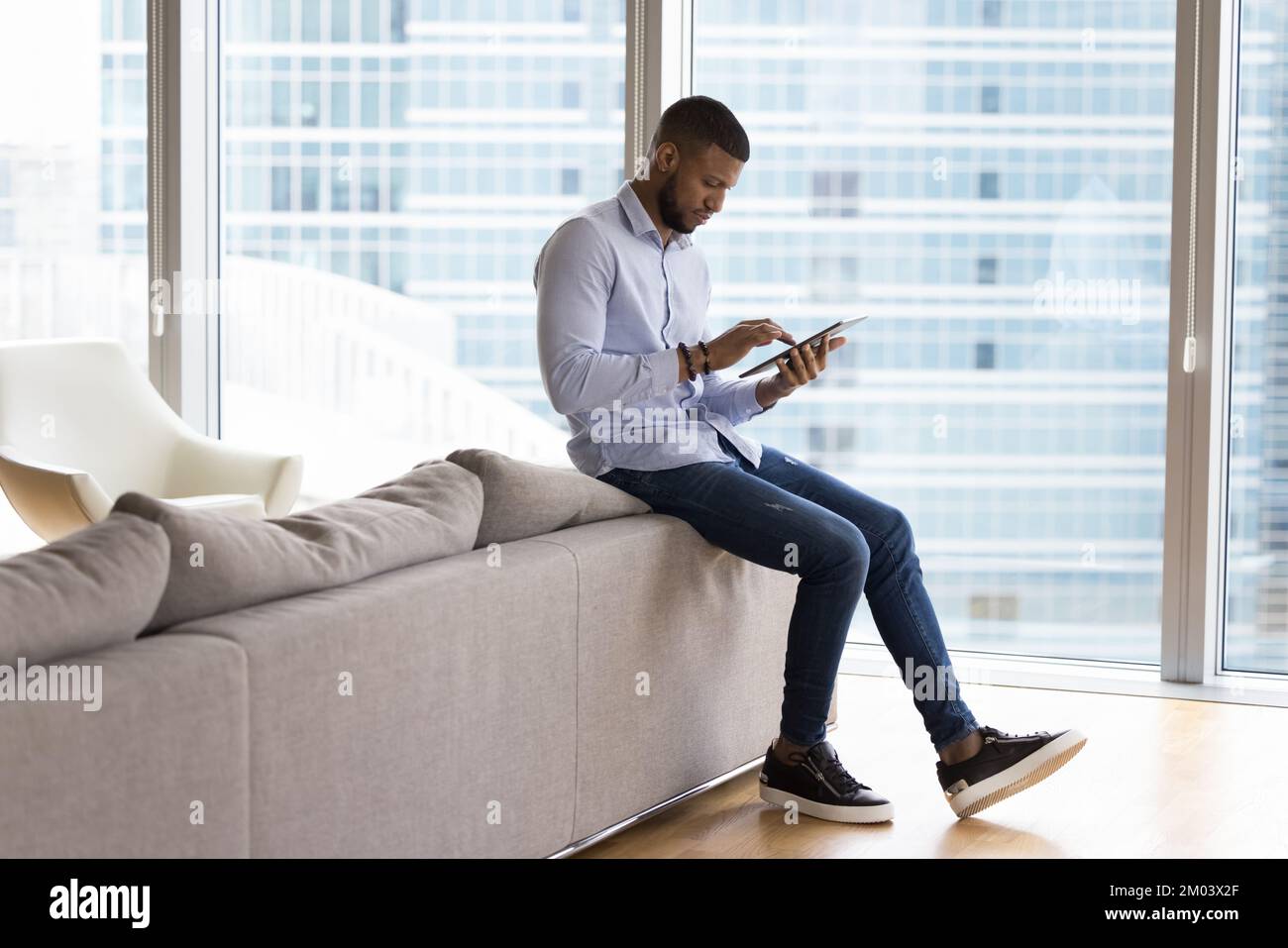 Focused millennial African tablet user man reading text on screen Stock Photo