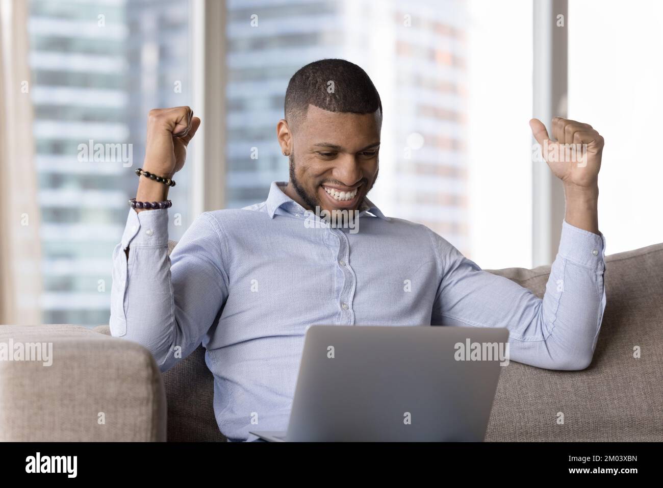 Cheerful happy young millennial Black business man looking at laptop Stock Photo