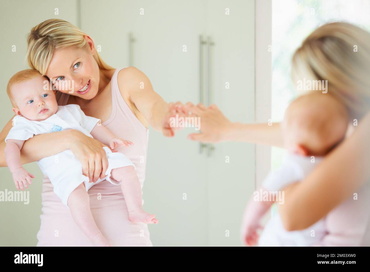 Look how cute you are. A cute baby girl looking at herself in the mirror while her mom points. Stock Photo
