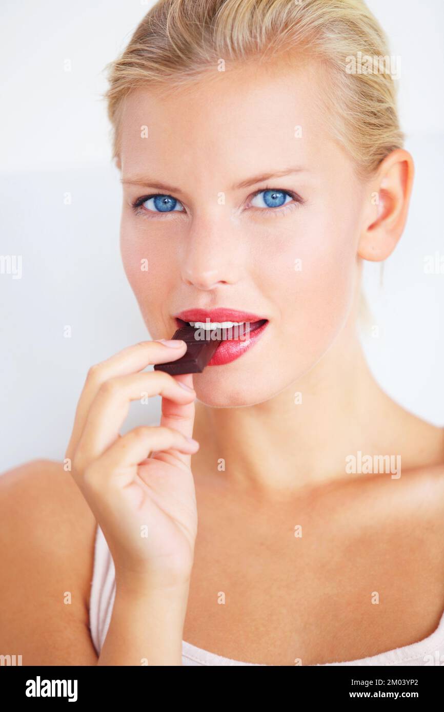 Indulging in a little treat. Smiling young woman enjoying a delicious piece of chocolate. Stock Photo