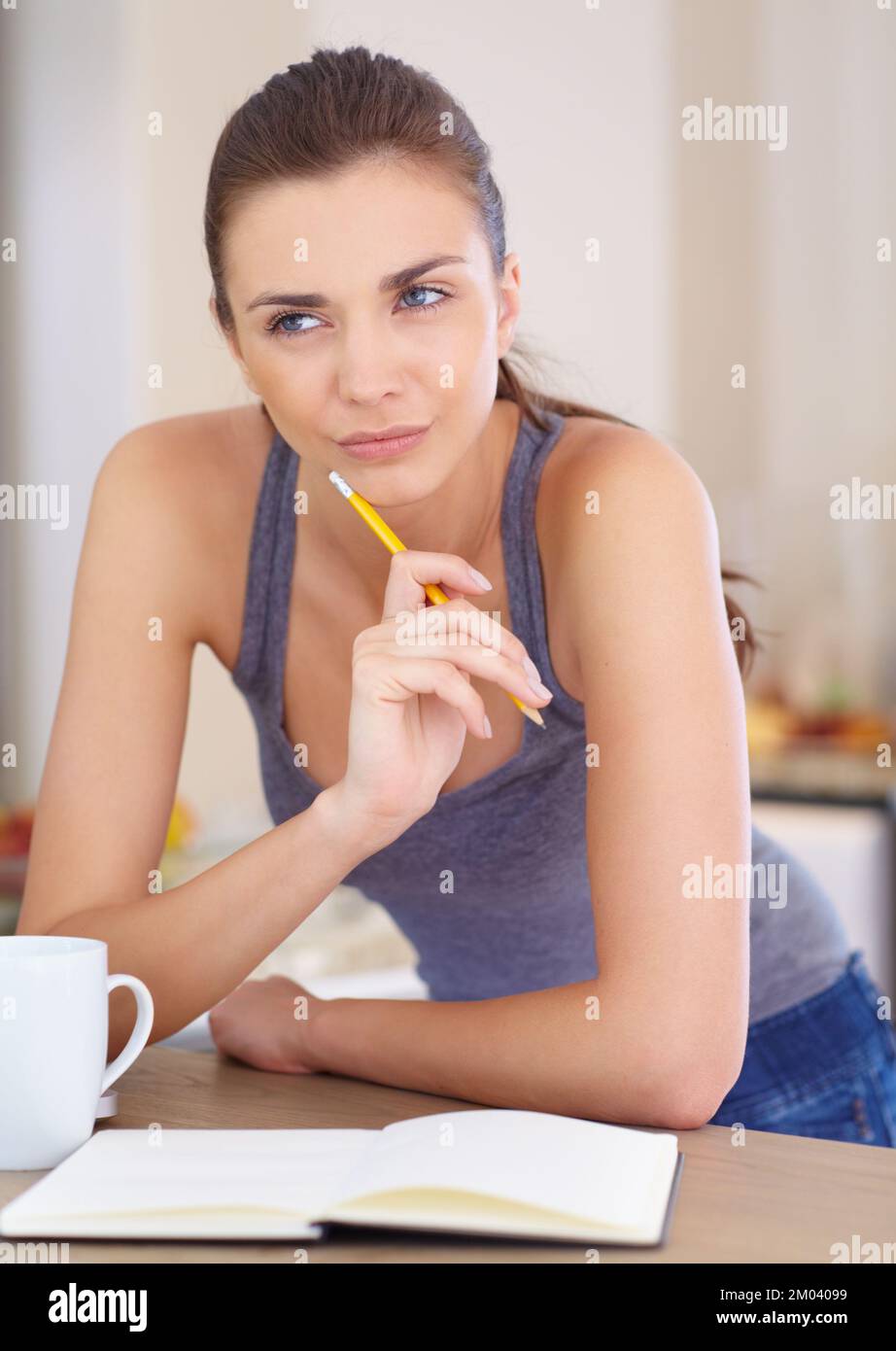 Thinking of the right words...An attractive young woman looking thoughtful while writing in a book. Stock Photo