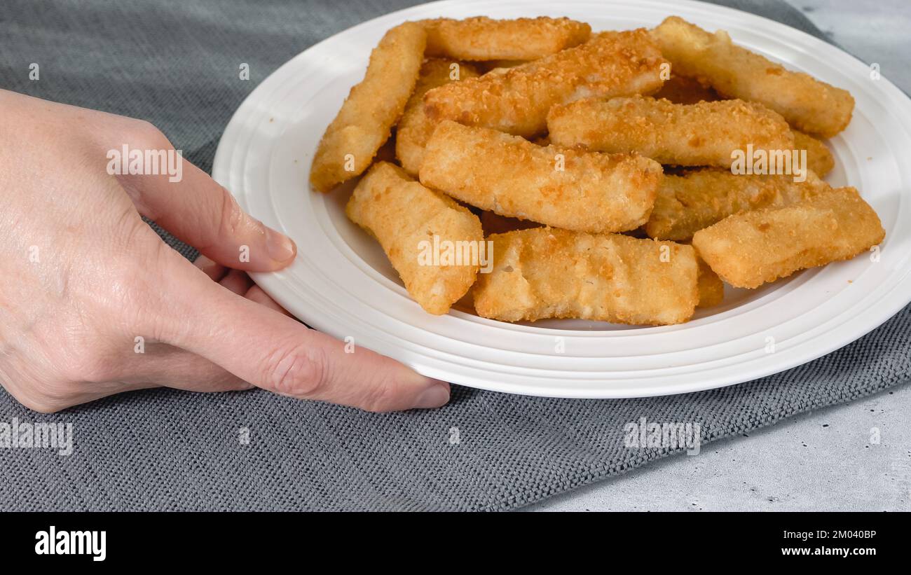 Fish sticks in a crunchy golden breading close-up on white plate on the kitchen table Stock Photo