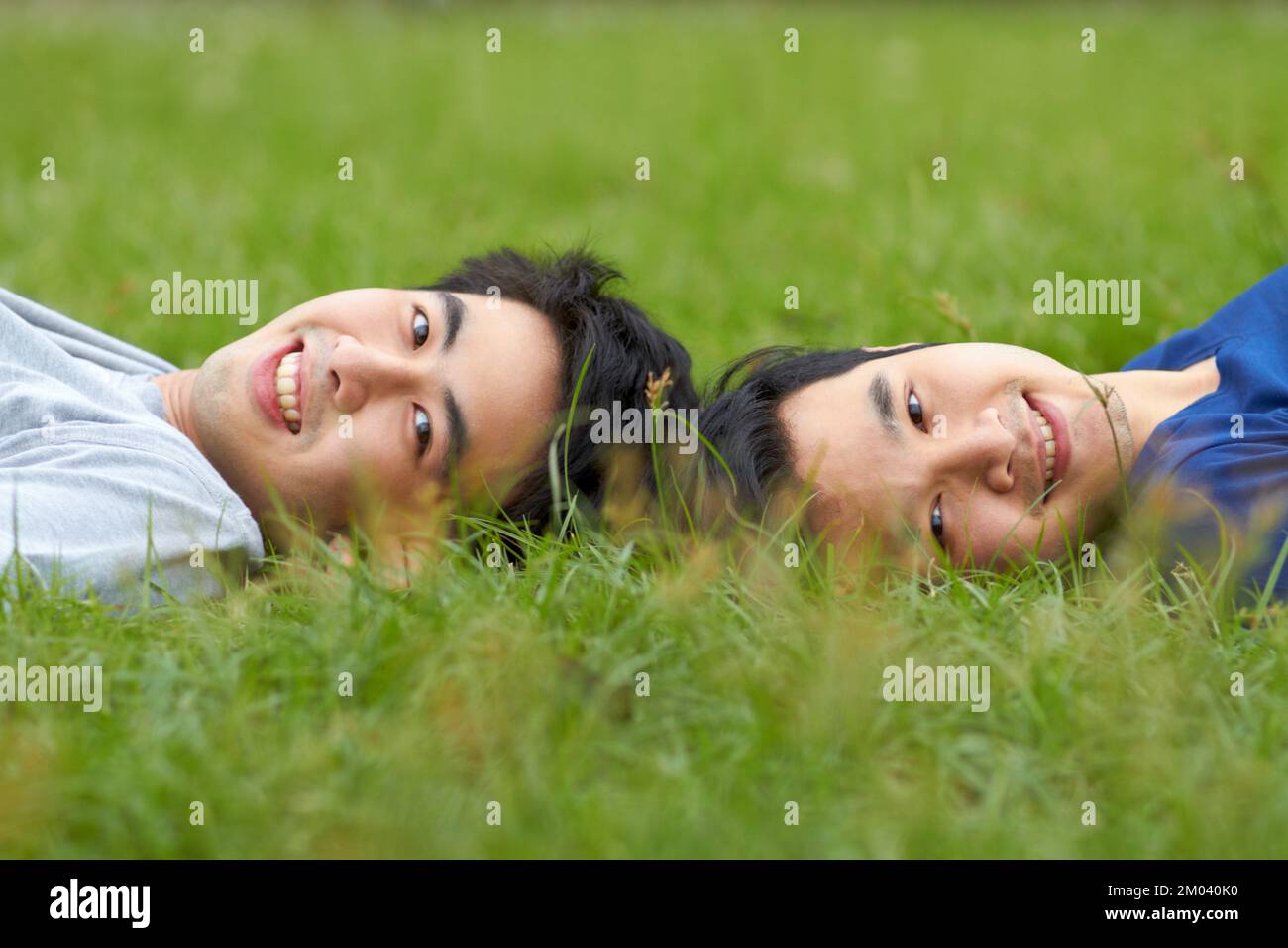 Sharing the same thoughts and dreams. Cute young gay Asian couple smiling together while lying on the grass. Stock Photo