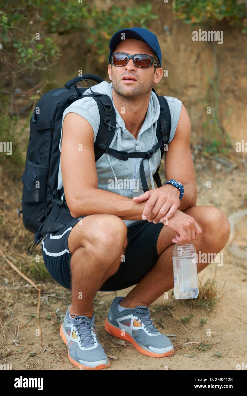 Taking a moment to catch his breath. Young hiker taking a break and holding a water bottle. Stock Photo