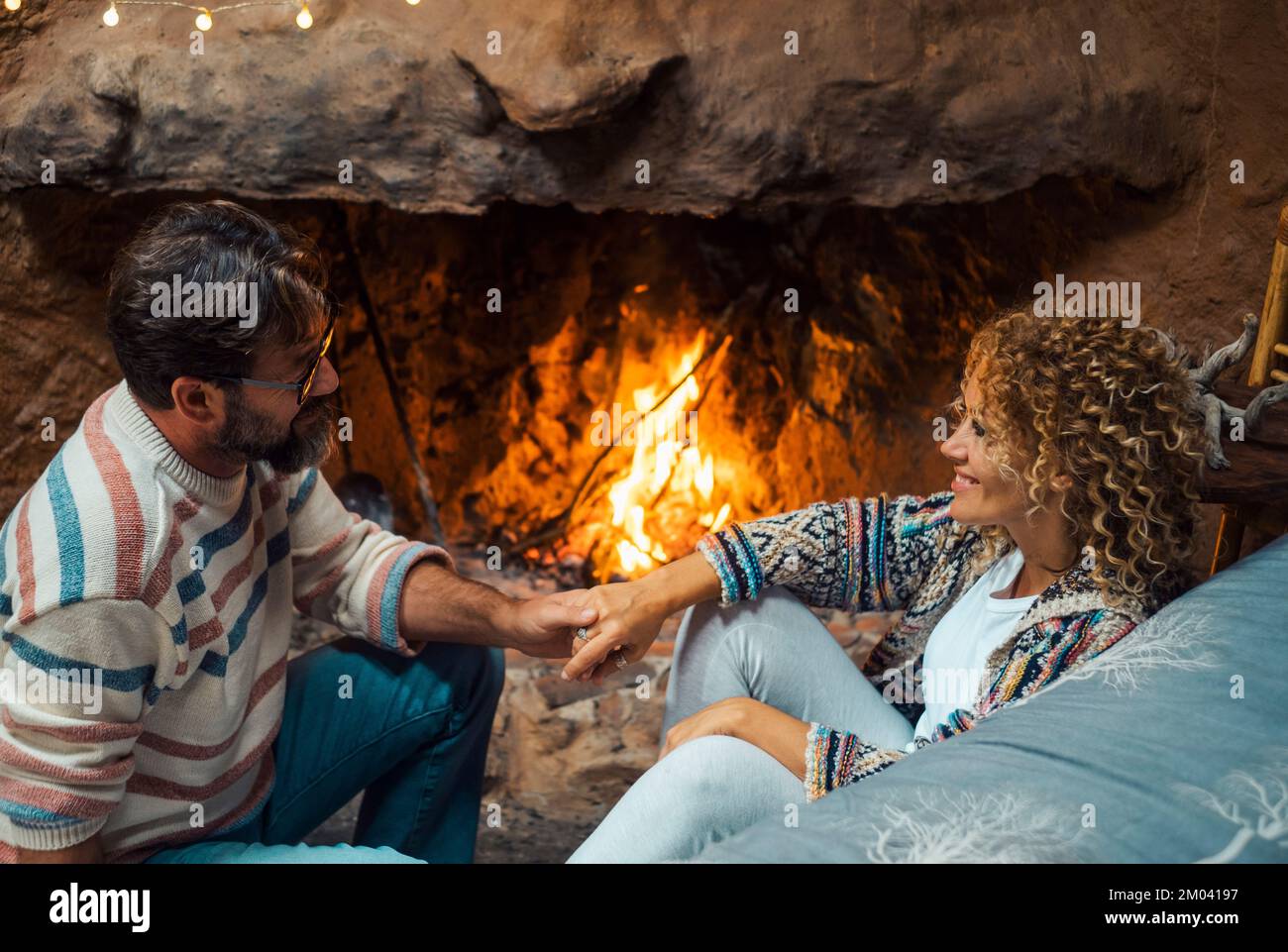Happy young couple in romantic leisure activity at home enjoying fireplace to heating home. Romance and love with man and woman in winter holiday chal Stock Photo