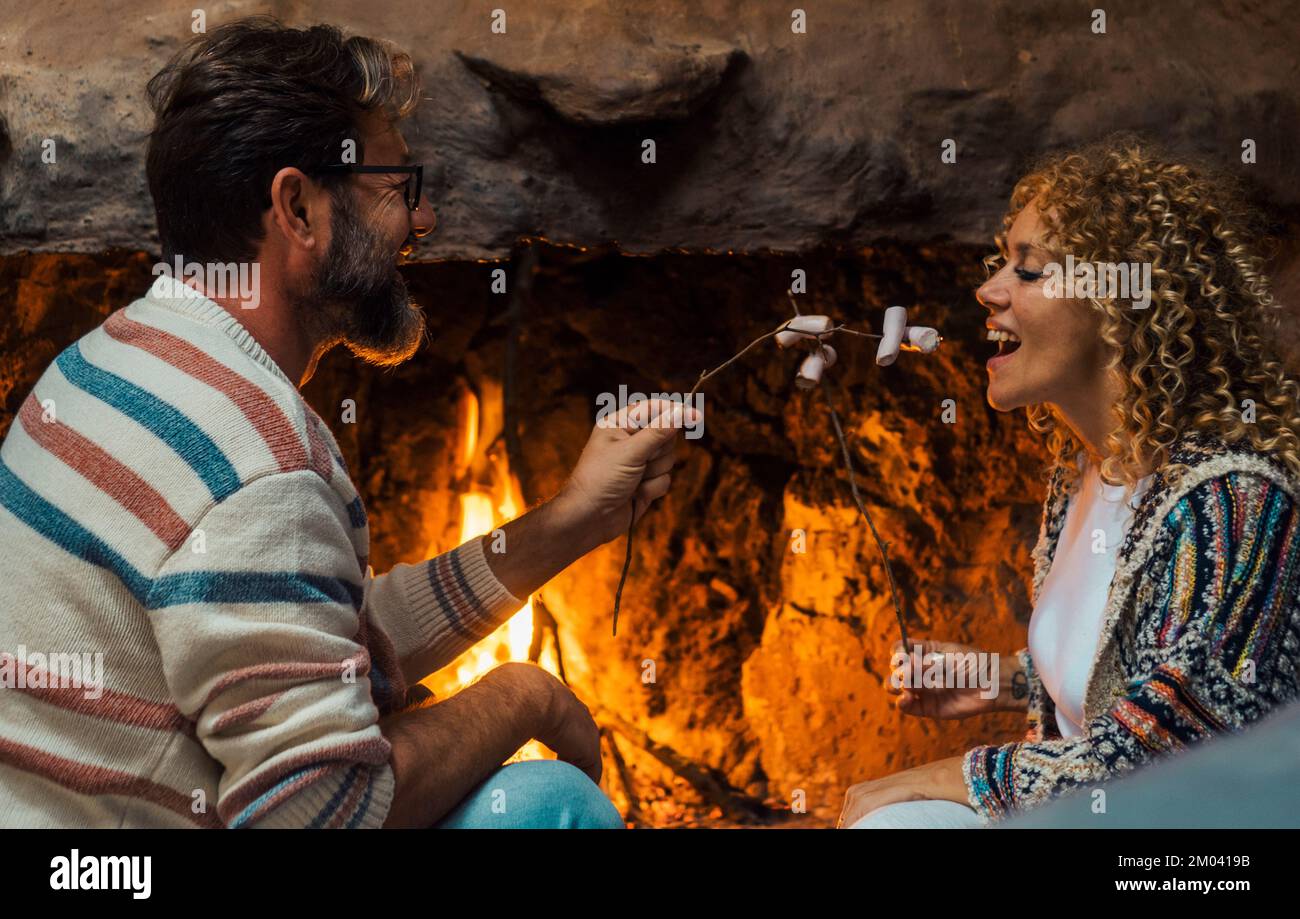 Banner with happy couple in love enjoying romantic indoor leisure activity together cooking marshmallows at the fireplace at home. Happy joyful people Stock Photo