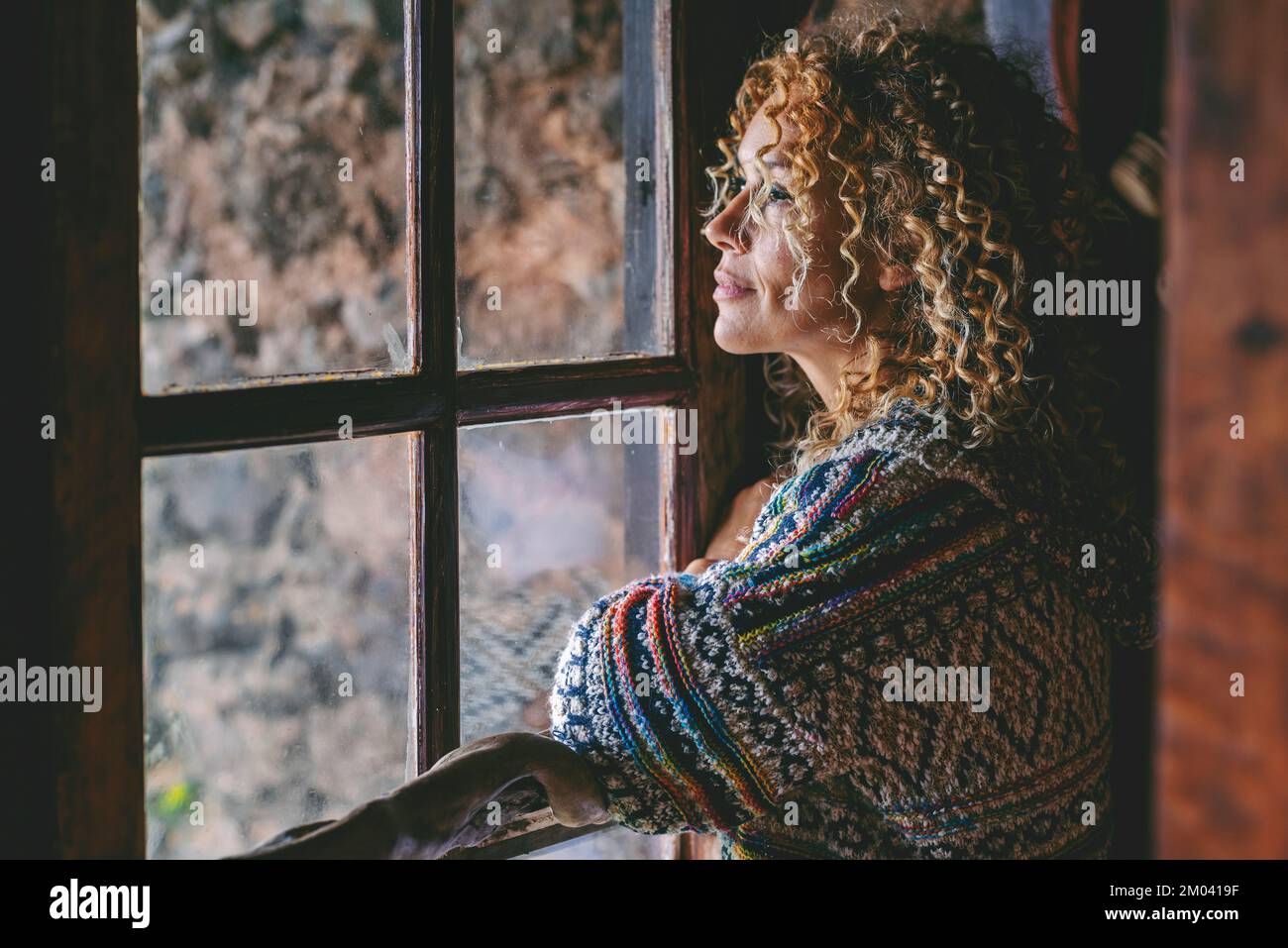 One alone woman standing at home near the window looking outside and thinking. Single female people lifestyle. Waiting friends and thoughts. Young lad Stock Photo