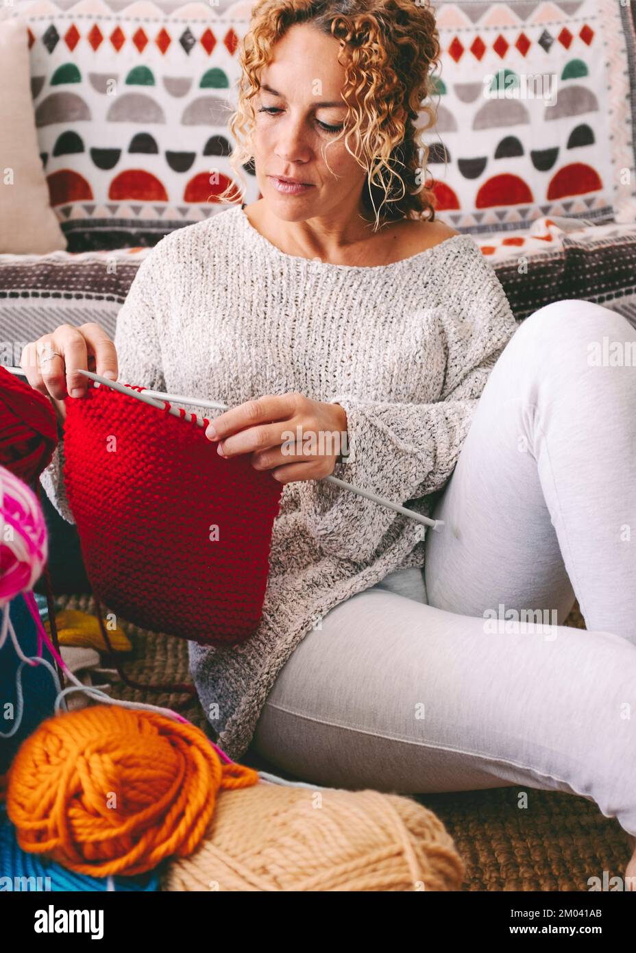 Real life scene portrait of middle age young woman doing knit work t home sitting on the floor. People and hobby. Indoor leisure activity female knitt Stock Photo