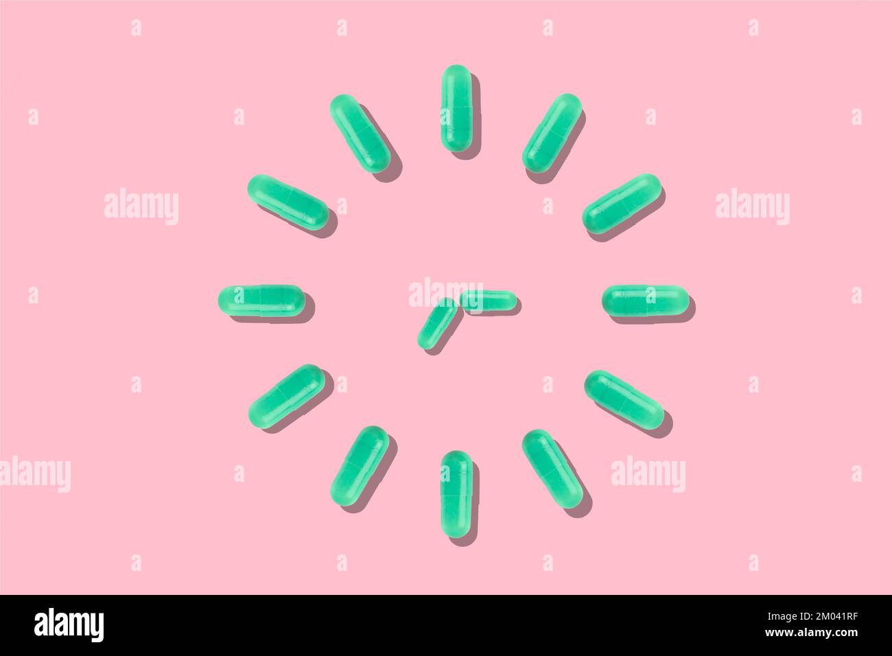 Green capsules placed together in the shape of a clock on a pink background. Photo of medical products with 3d illustration. Stock Photo