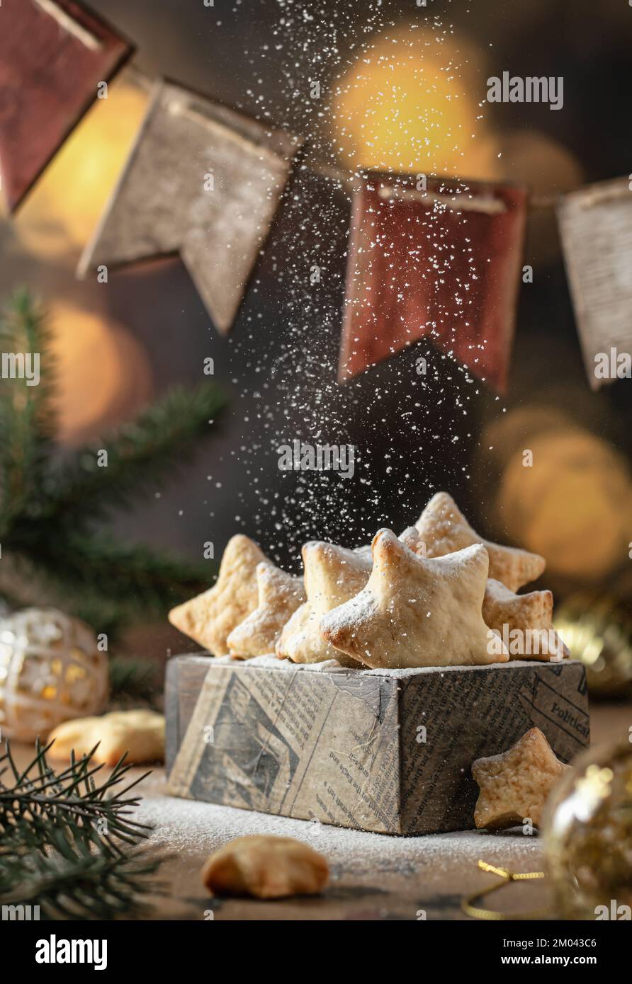 Homemade Christmas shortbread star shape cookies with powdered sugar in wooden box, with green fir tree, garland of wooden flags and golden bokeh Stock Photo