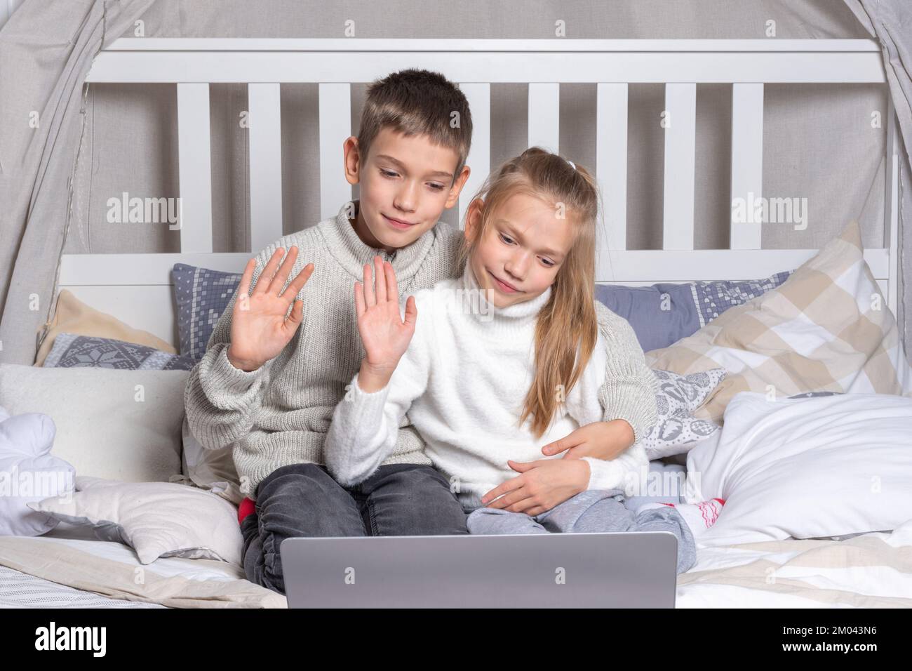 Preschool children communicate via video link via laptop and wave to relatives or friends at home. Boy and girl brother and sister congratulate on the Stock Photo