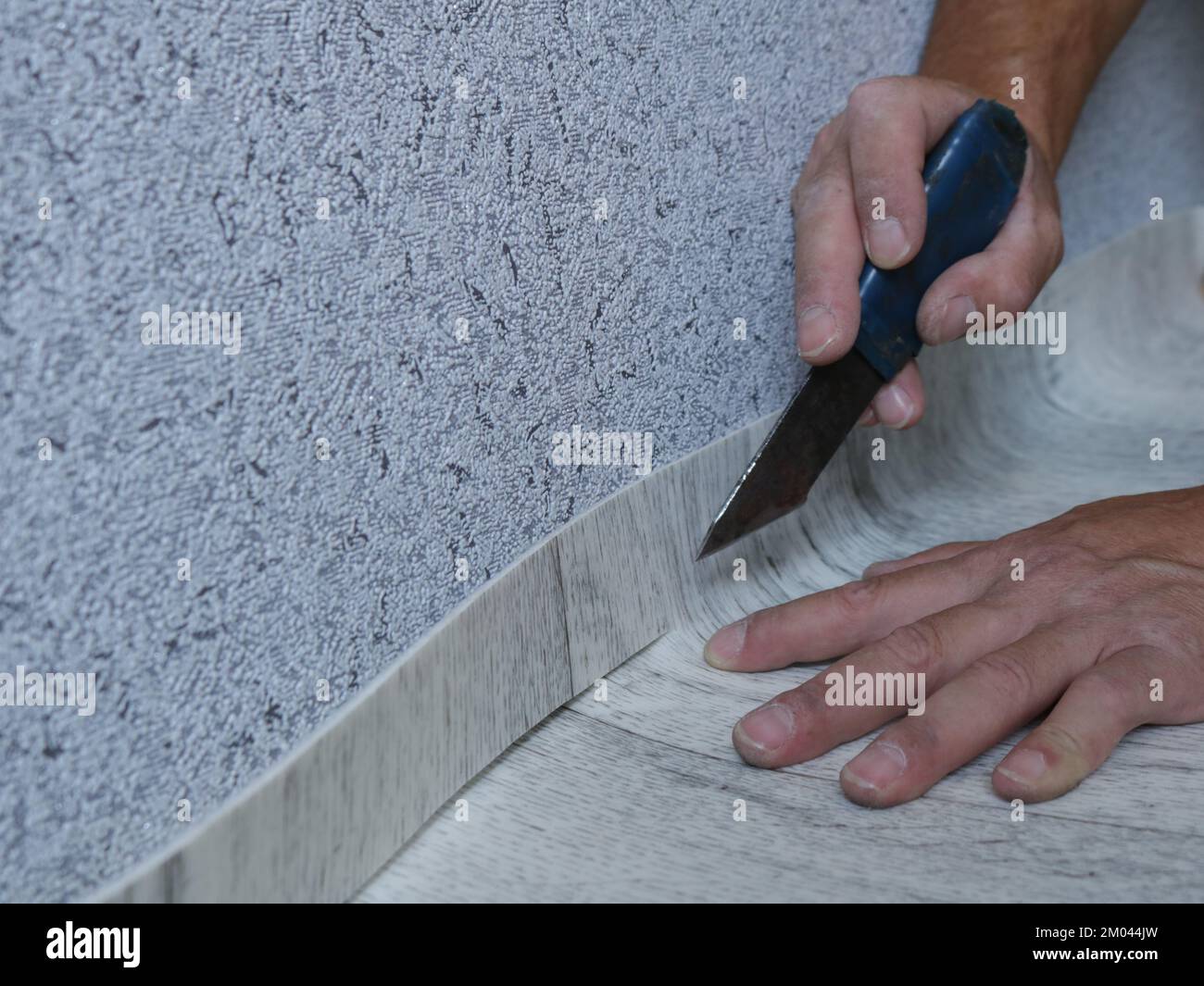 cutting linoleum with a short knife at the junction of the floor and wall, fitting the carpet to the size of the room, male hands cut light linoleum Stock Photo