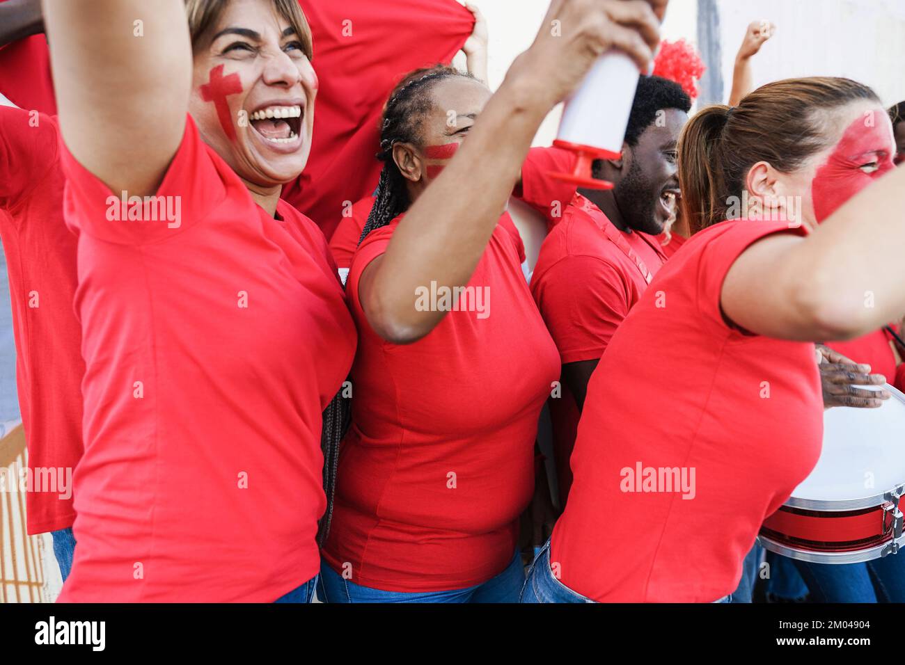 Multiracial red sport fans screaming while supporting their team - Football supporters having fun at competition event - Focus on african woman ear Stock Photo