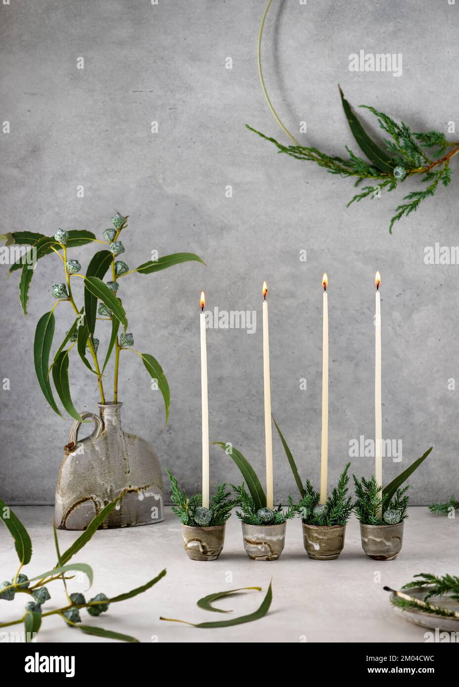 4. Advent. Christmas decor with white narrow candles, eucalyptus leaves and fruits in four ceramic mugs. Handmade home decoration. Selective focus. Stock Photo