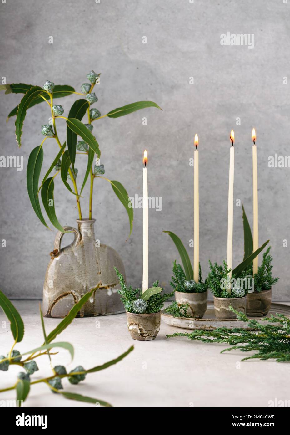 Beautiful winter floristic arrangement with white narrow candles, eucalyptus leaves and fruits in four ceramic mugs. Handmade Christmas home decor Stock Photo