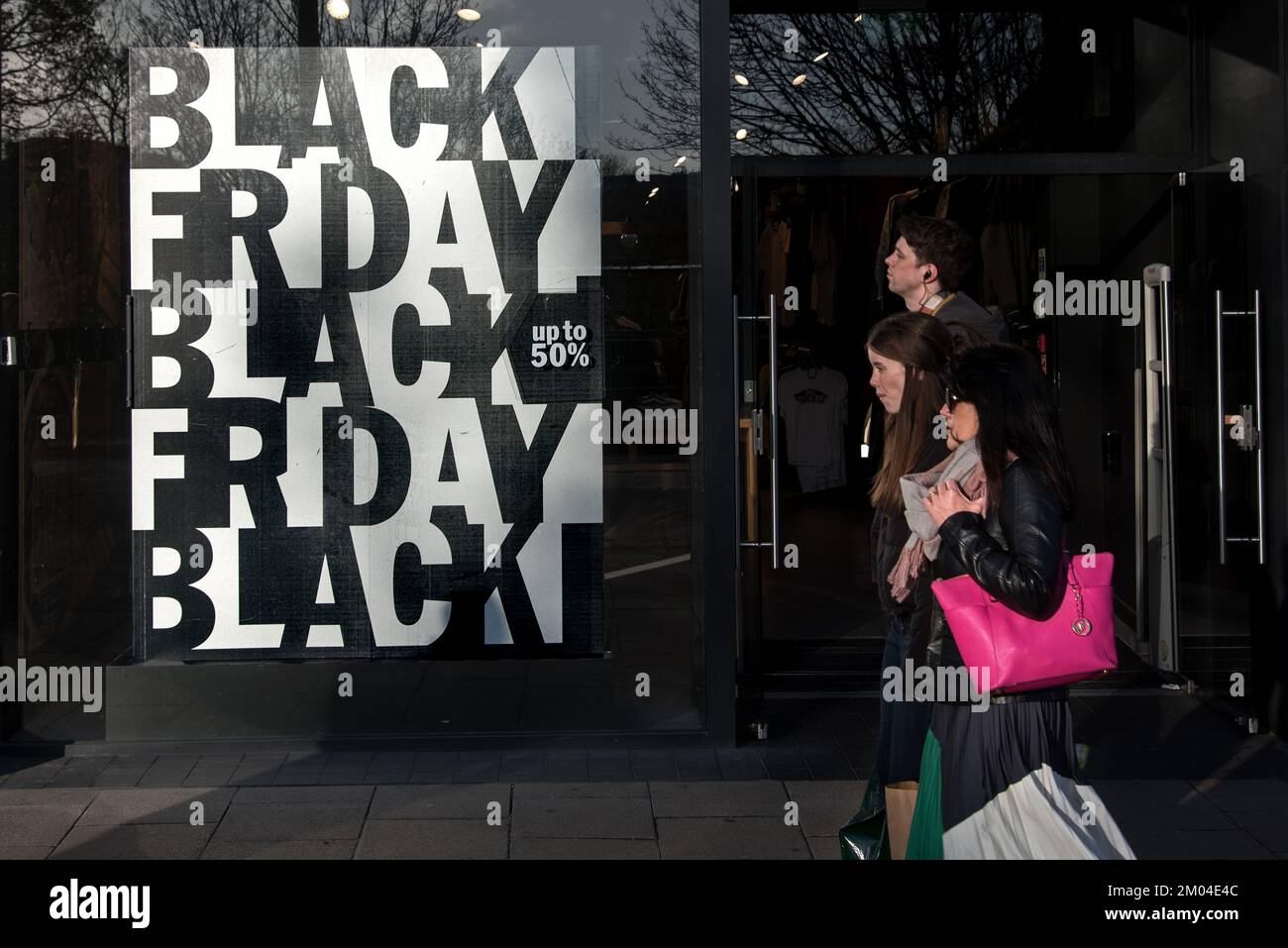 People walking by Black Friday posters in the window of a shop on Princes Street, Edinburgh, Scotland, UK. Stock Photo
