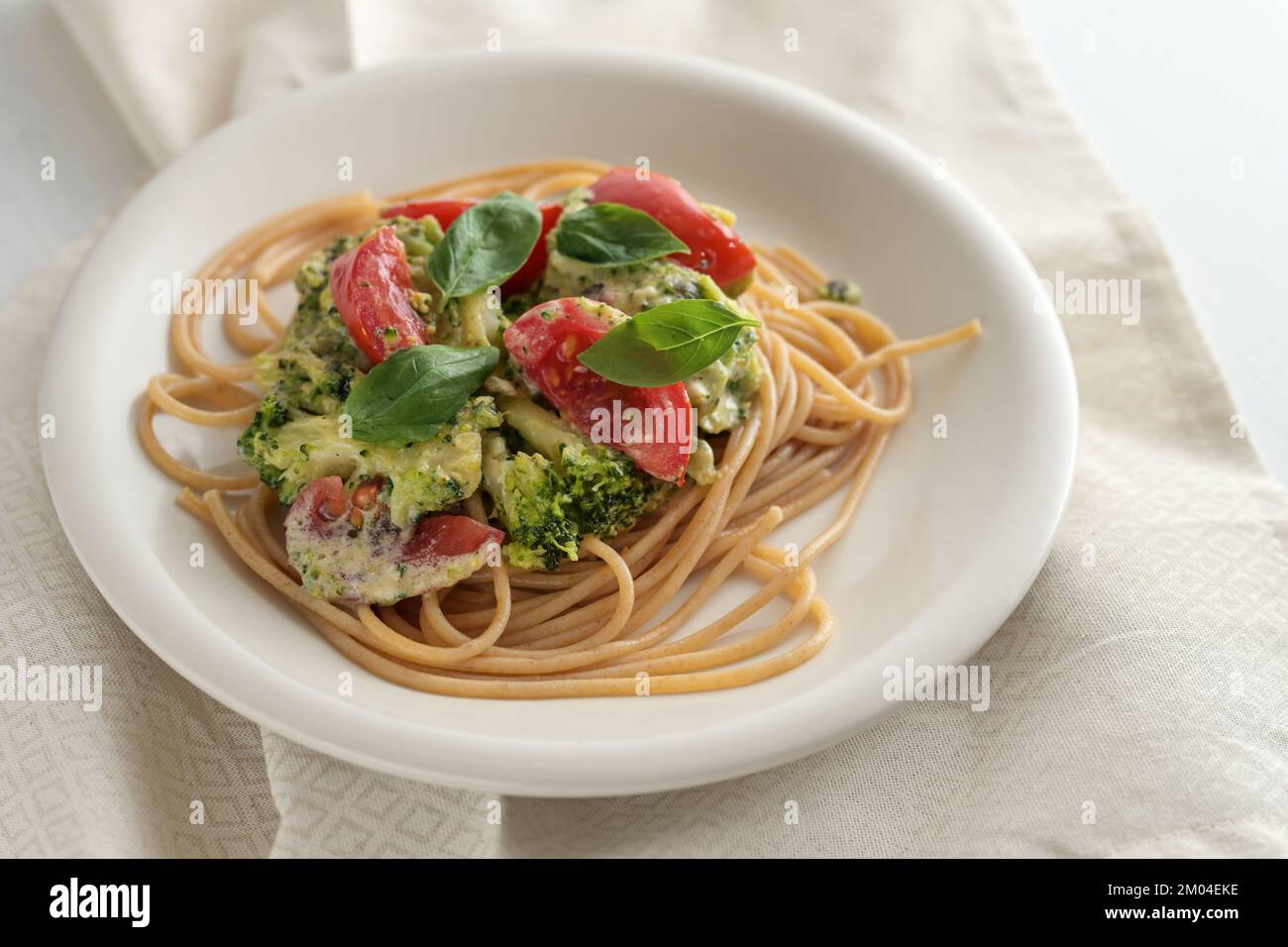 Whole grain spaghetti with broccoli and tomato cream sauce and basil garnish, healthy vegetarian