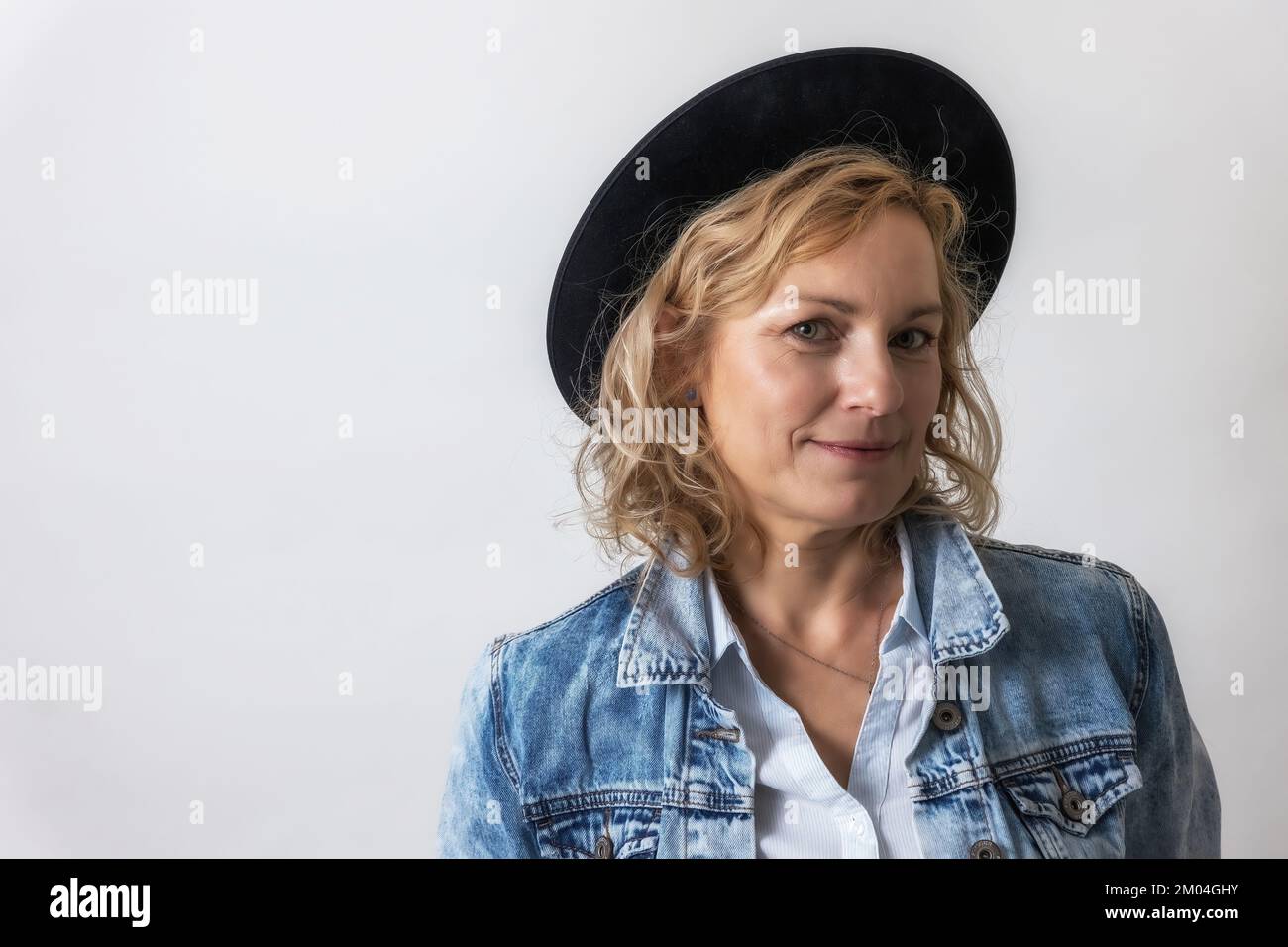 Portrait of smiling middle age woman with black hat on the light background. Stock Photo