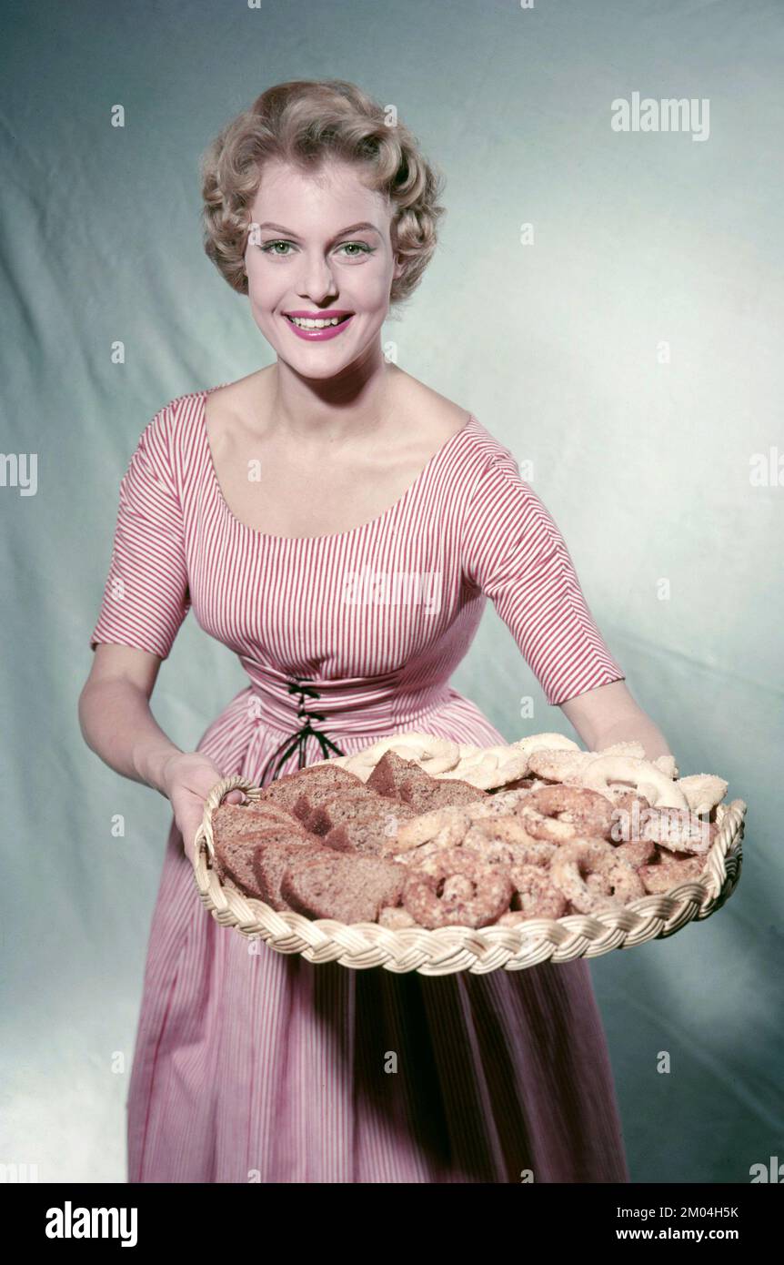 In the 1950s. A woman in a patterned dress is holding a tray with freshly baked cookies and buns. Sweden 1958 Stock Photo