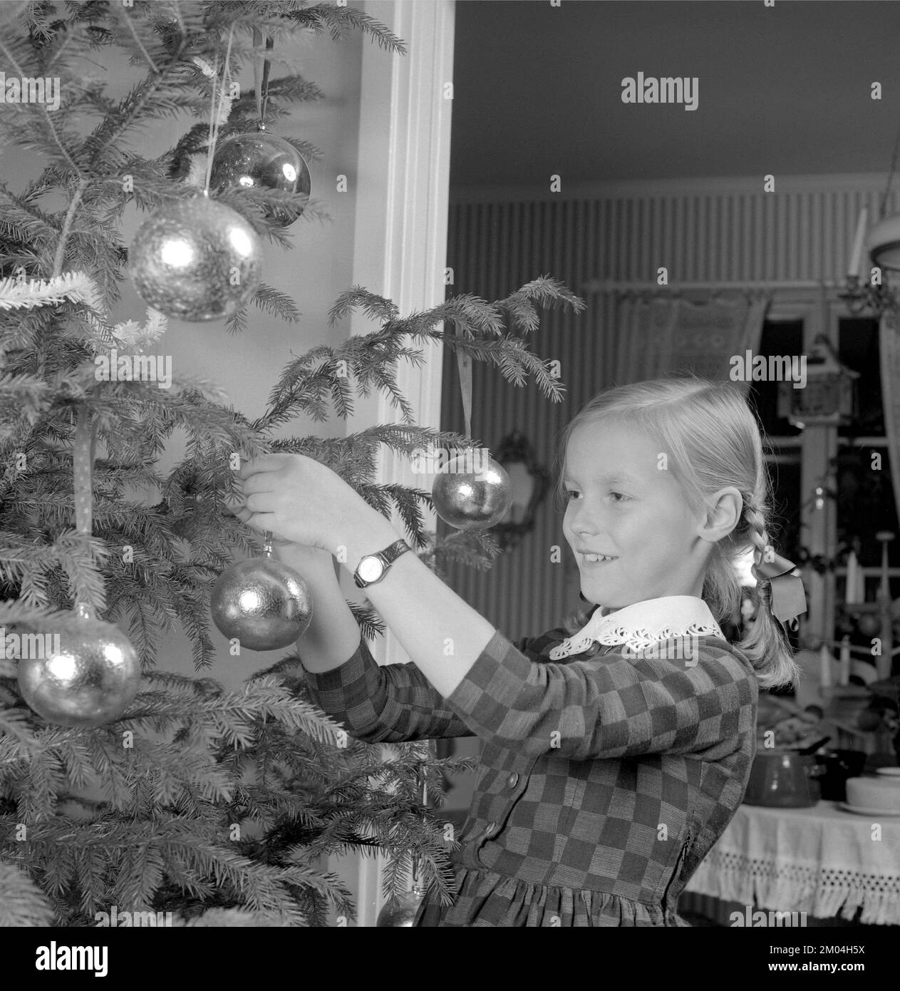 Christmas in the 1960s. A young girl is standing by the christmas tree decorating it. Sweden 1963 Ref 4827 Stock Photo