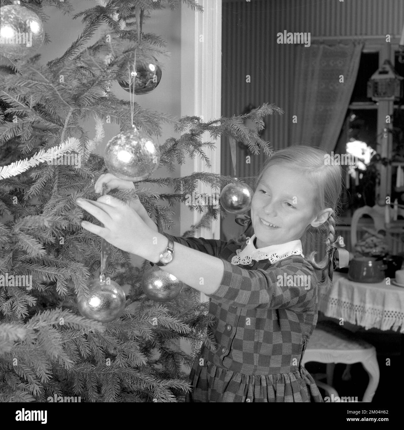 Christmas in the 1960s. A young girl is standing by the christmas tree decorating it. Sweden 1963 Ref 4827 Stock Photo