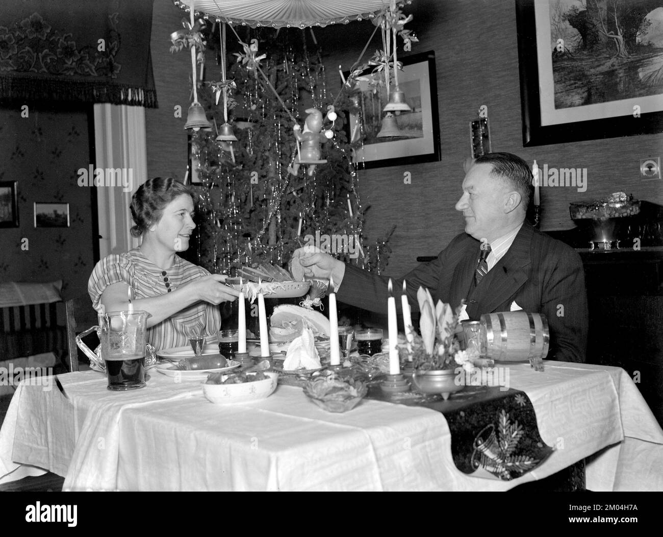 At christmas in the 1940s. A couple is seen having their christmas dinner at a table in a christmas decorated room including a christmas tree. Sweden december 1940 Kristoffersson 42-11 Stock Photo