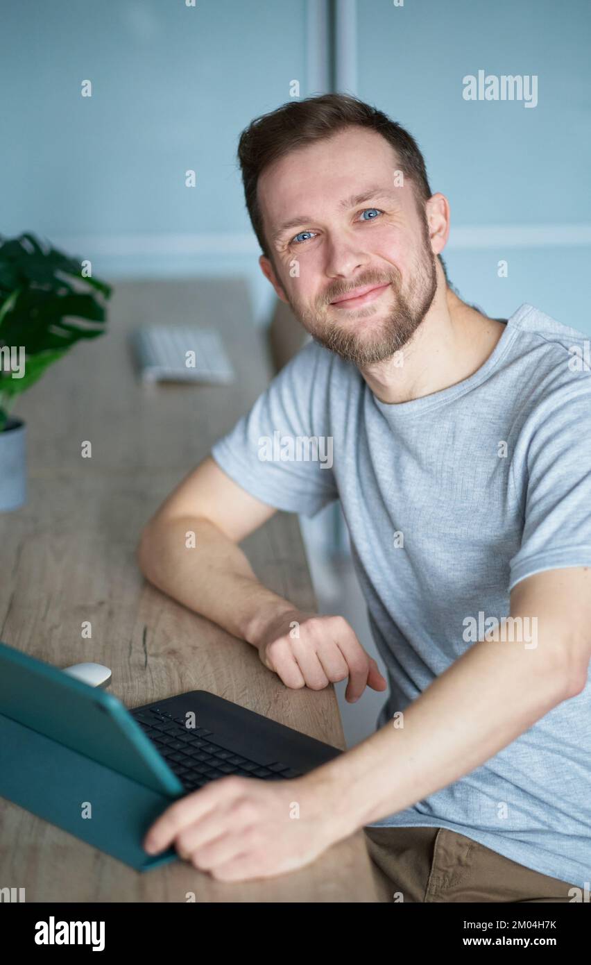 Attractive caucasian male freelancer or entrepreneur concept. Successful bearded man using tablet computer for business sitting at home office. High quality vertical photo Stock Photo