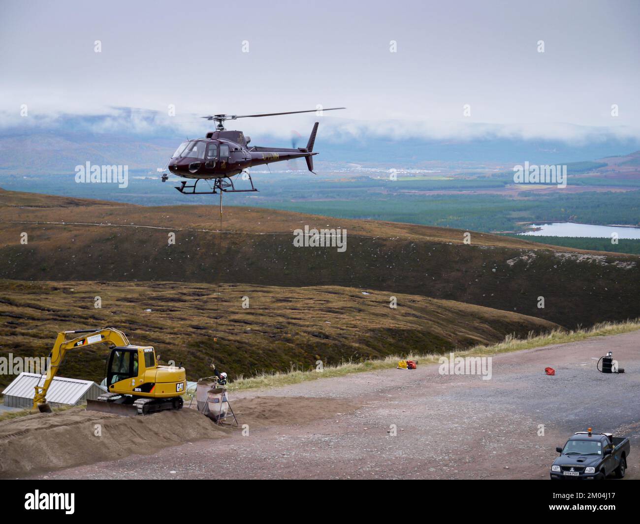 Aviemore, Scotland UK. Taken on 14 October 2009. Helicopter lifts bags of stone in the air. Man attaching rope to tonne bags of stone. Stock Photo