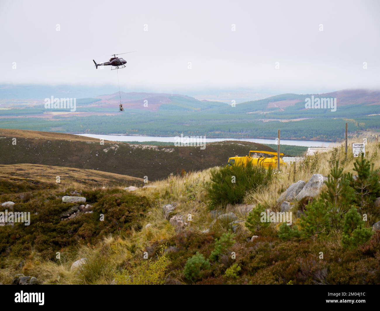 Aviemore, Scotland UK. Taken on 14 October 2009. Helicopter lifts bags of stone in the air. Man attaching rope to tonne bags of stone. Stock Photo