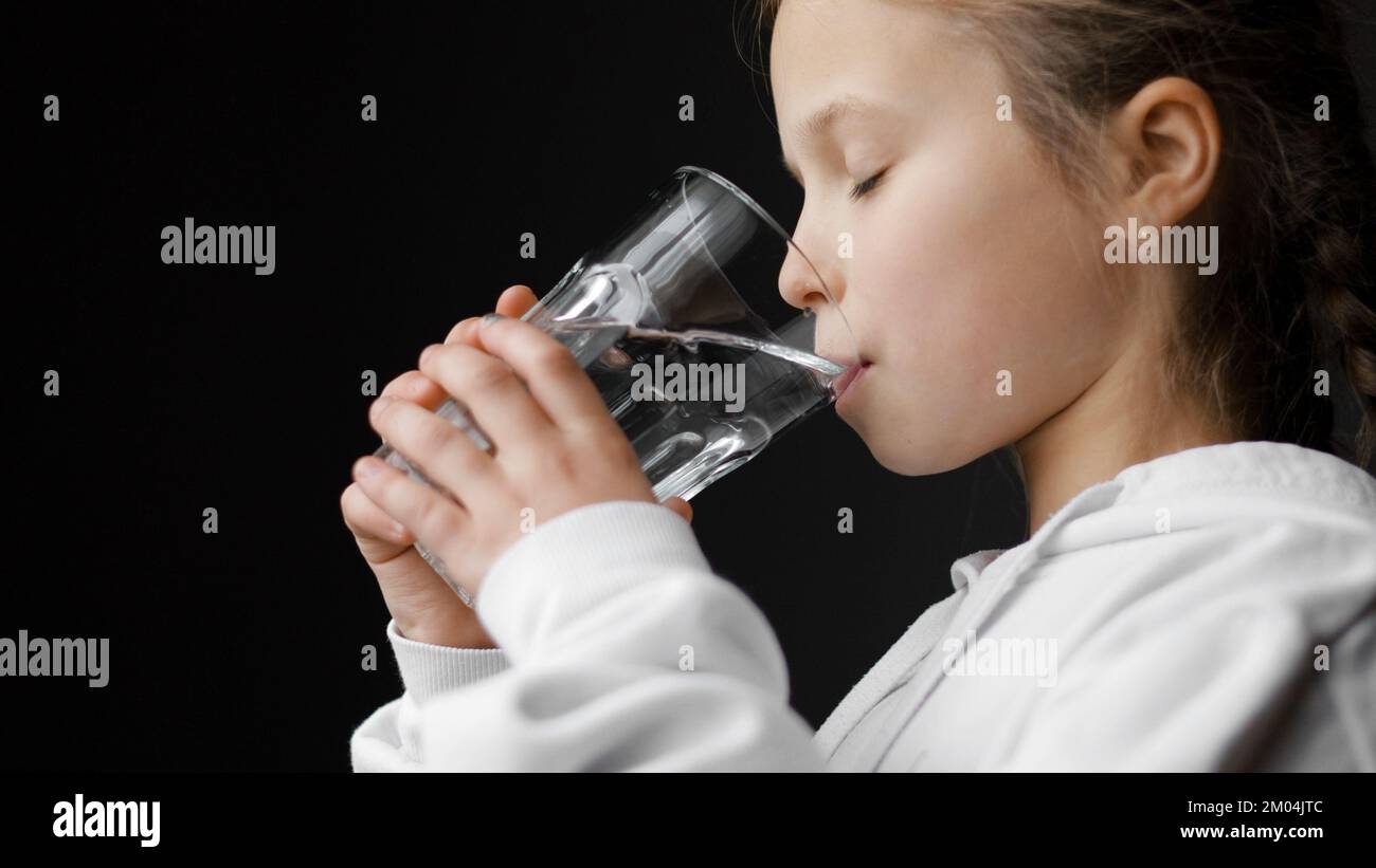 Water balance and children health care. Little girl drinks fresh transparent pure filtered mineral water at home. Thirsty dehydrated teenager holds gl Stock Photo