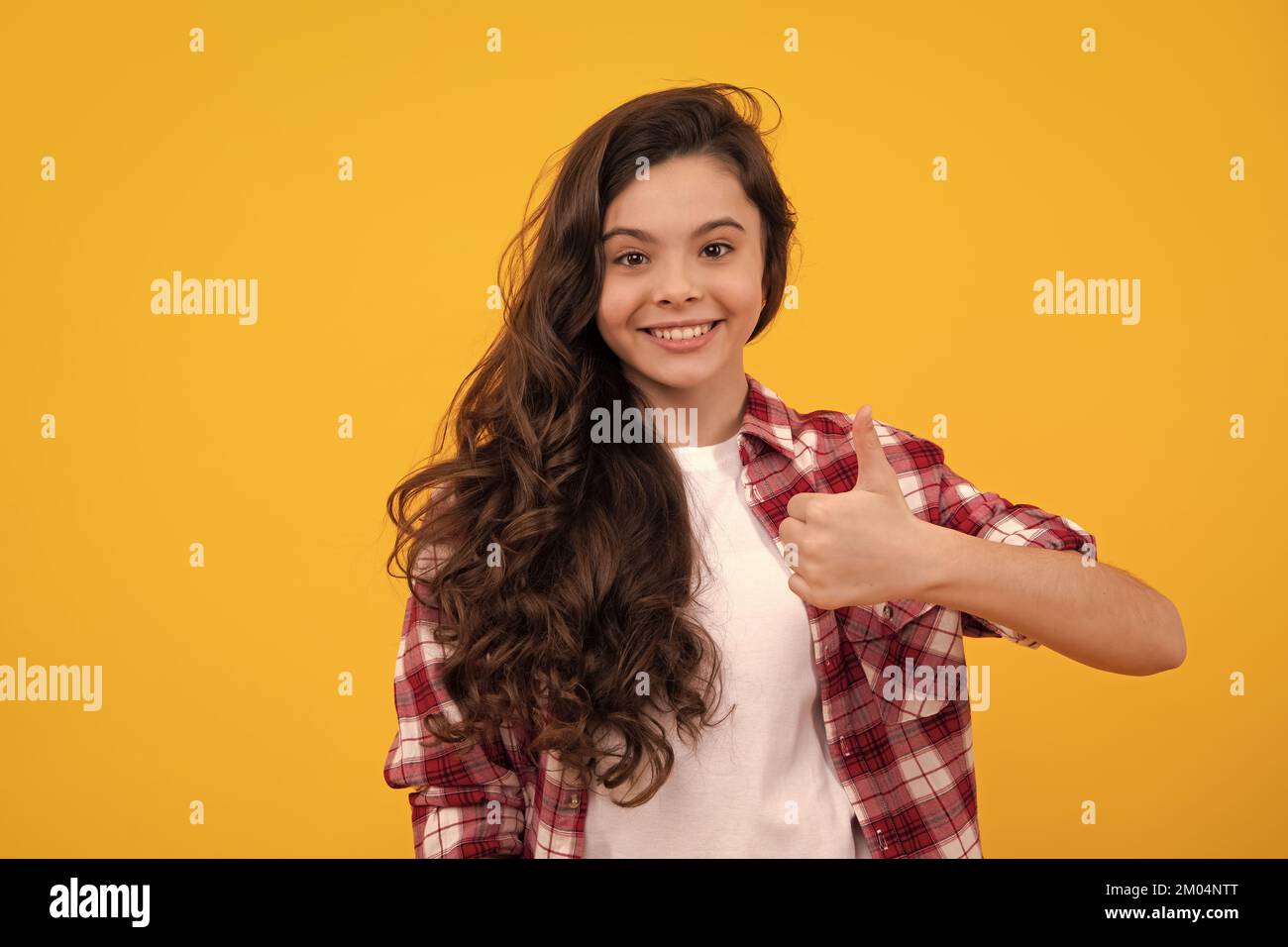 Happy teenager, positive and smiling emotions of teen girl. Optimistic cool teenager child girl with thumb up isolated on yellow background. Stock Photo