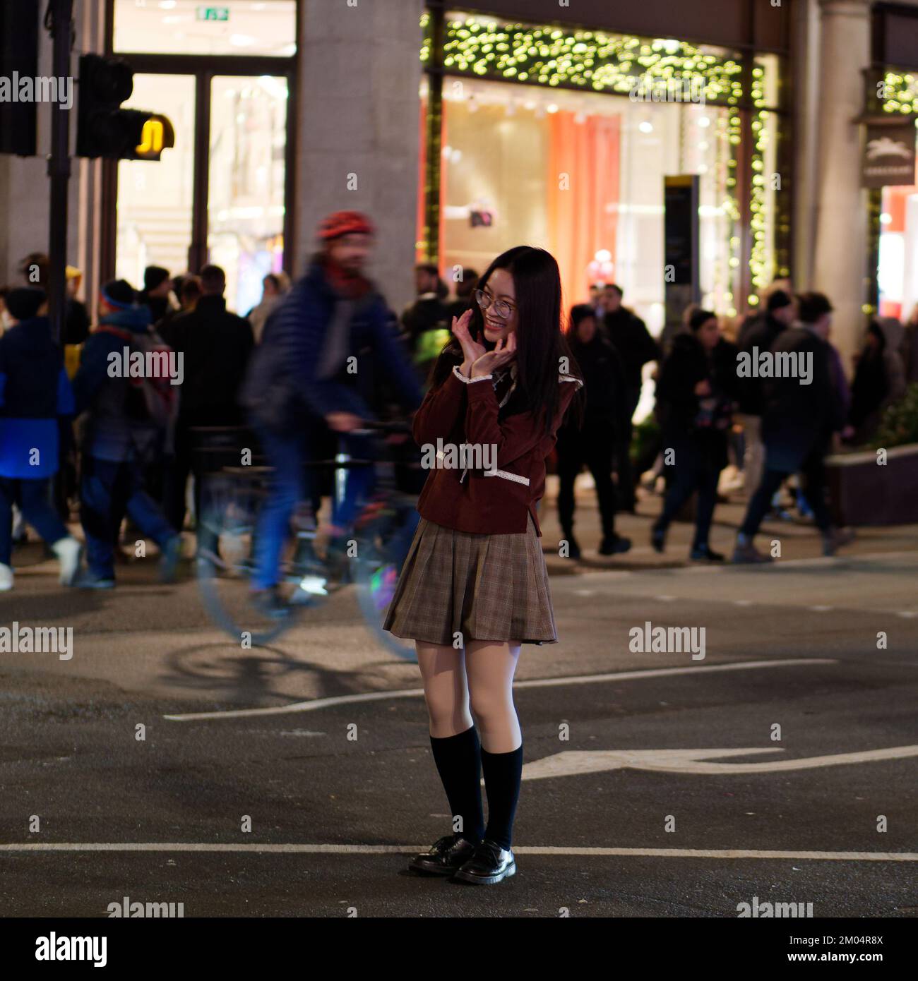 Spectacled asian Tourist poses and smiles for a photo on Regent Street wearing a mini skirt at night in winter. Stock Photo