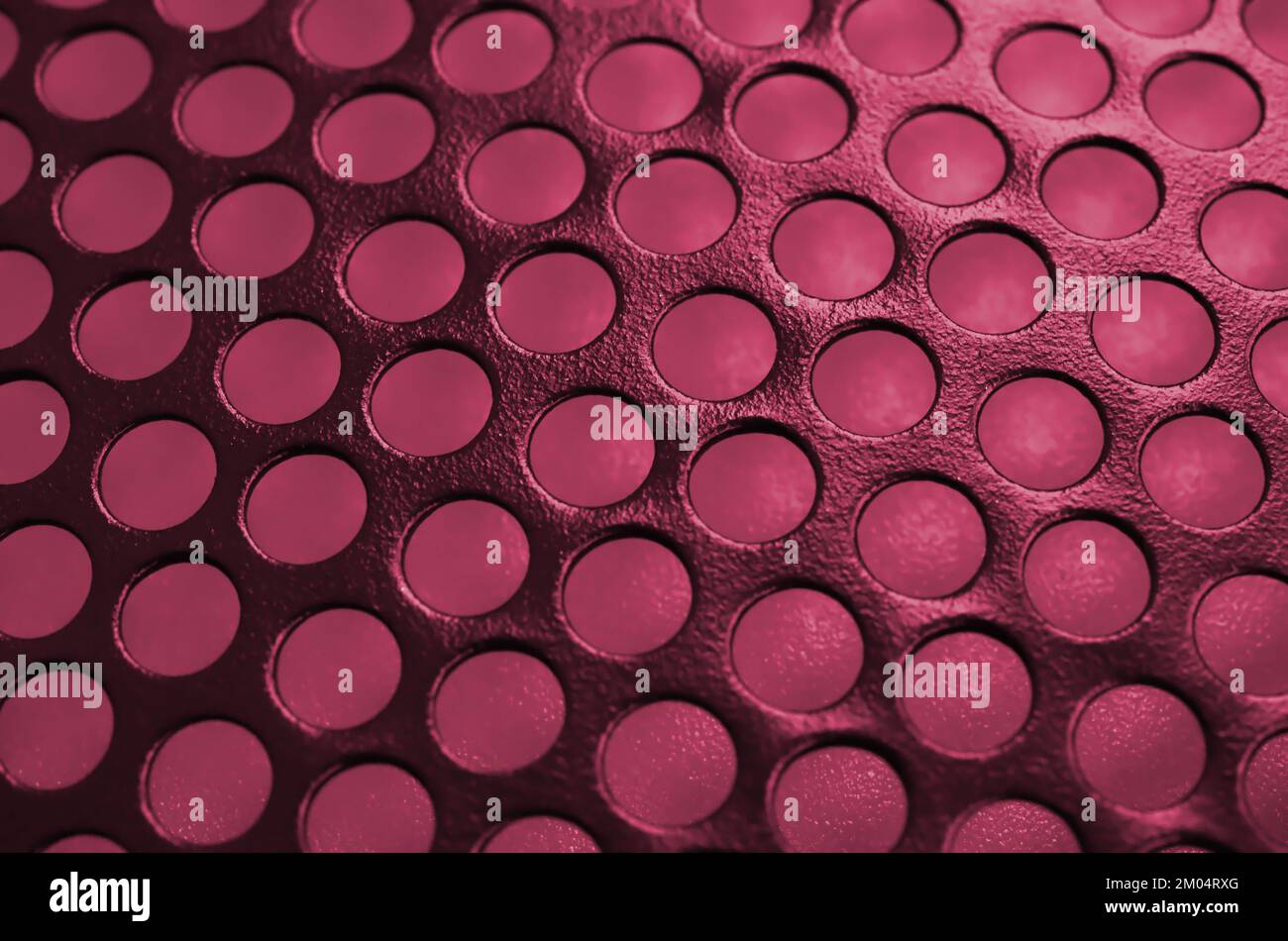 Black metal computer case panel mesh with holes on background. Abstract close up image. Image toned in Viva Magenta, color of the 2023 year Stock Photo