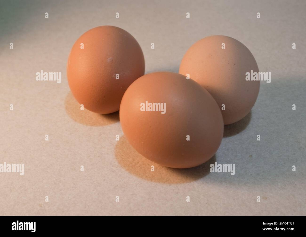 Three Brown Eggs Resting on a Beige Textured Surface Stock Photo