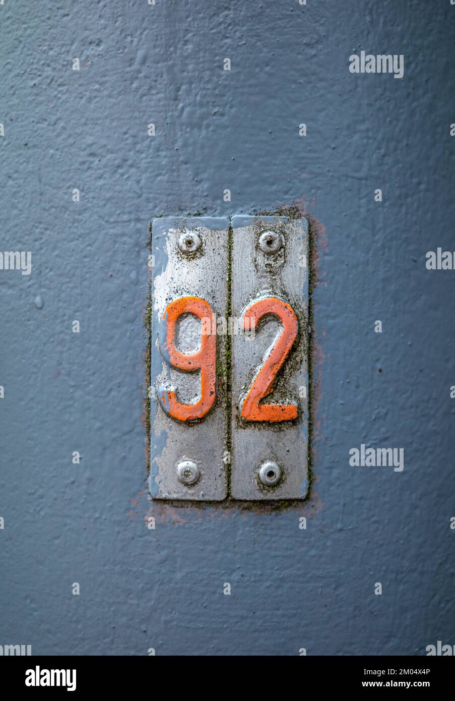 Orange number 92 on metal tiles on a gray background Stock Photo