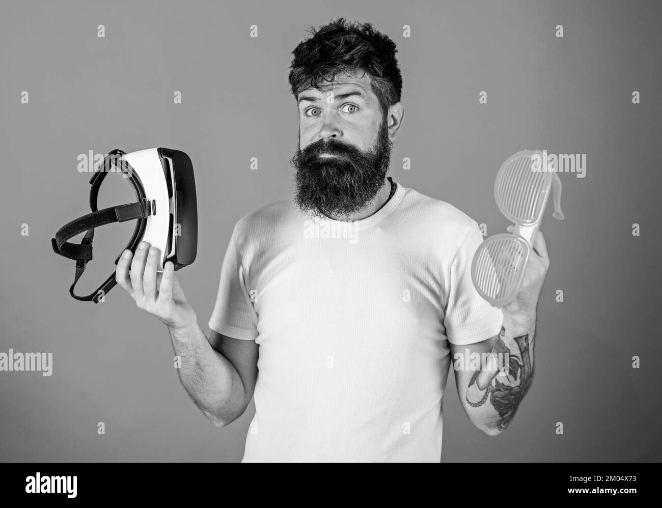 Man bearded hipster with virtual reality headset and louvered sunglasses on red background. Choice between reality and VR. Alternative reality. Man Stock Photo