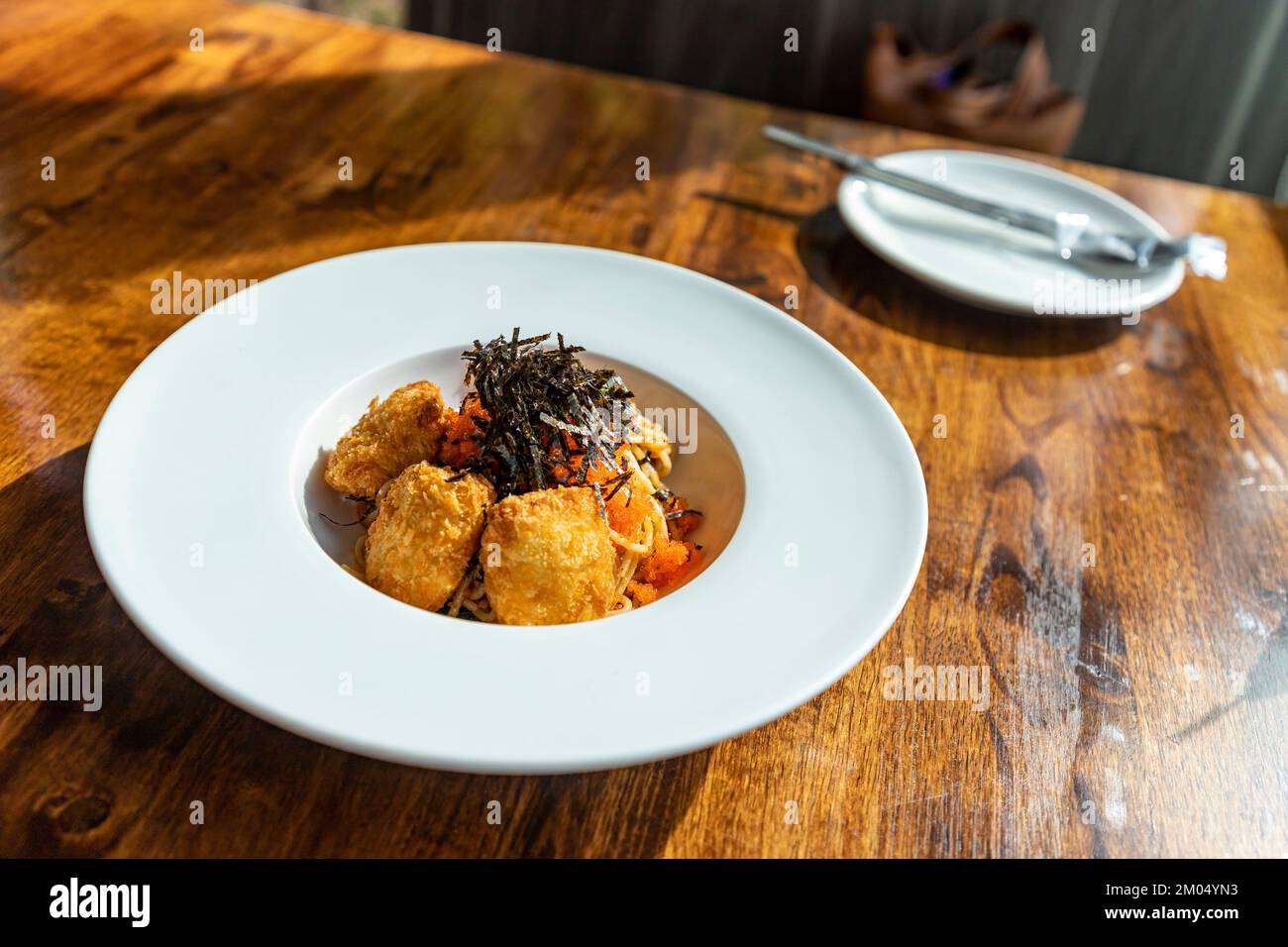 Fusion spaghetti topped with ebiko and seaweed Attached with fried breaded meat. in a white round plate on a wooden table There was sunlight shining t Stock Photo