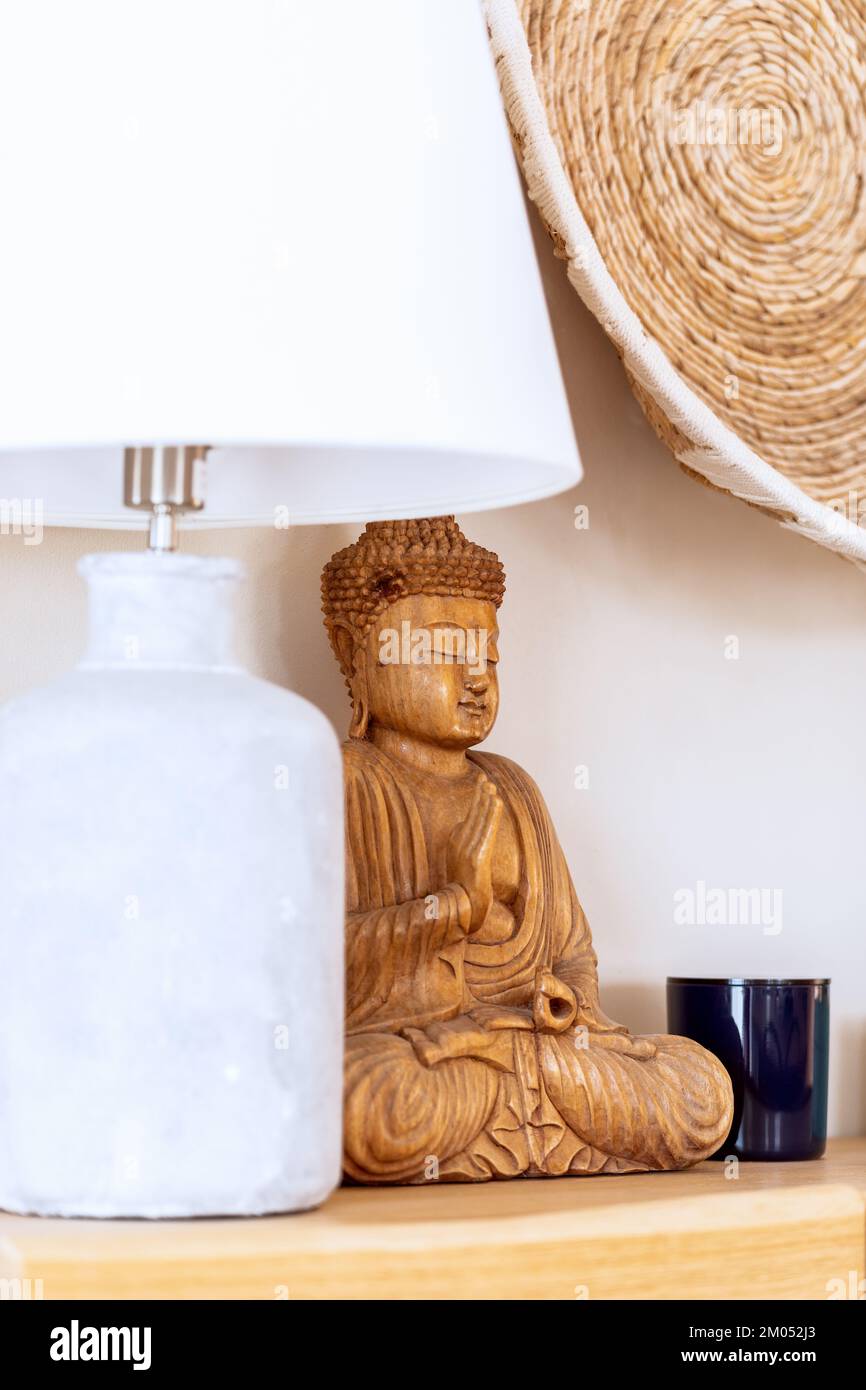 Decorative interior elements in ethnic style with white table lamp, wooden statue of Buddha and wicker wall planter (Vertical shot) Stock Photo