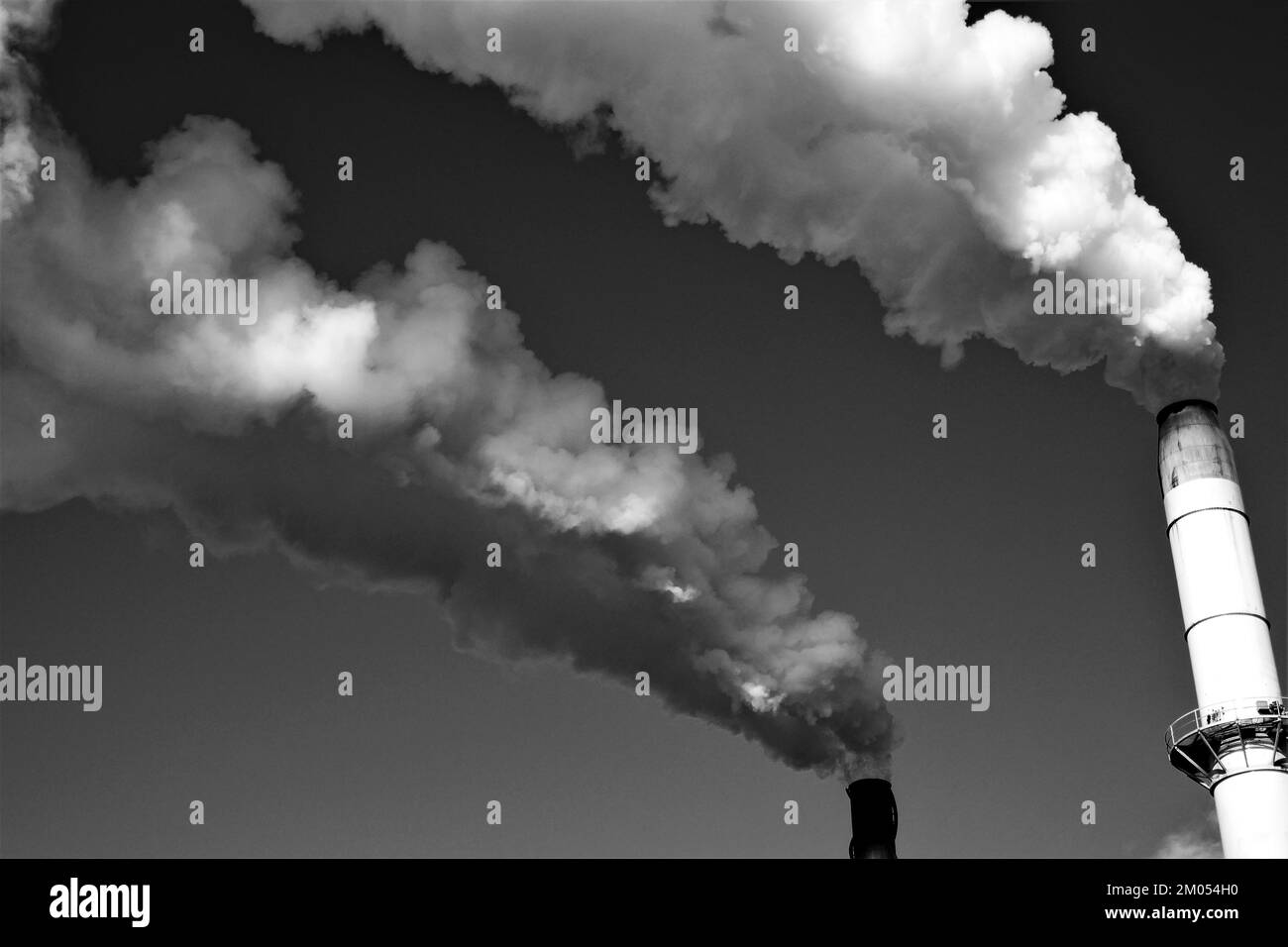 Smoke billowing out of tall industrial chimneys against a clear sky in Australia, in black and white Stock Photo