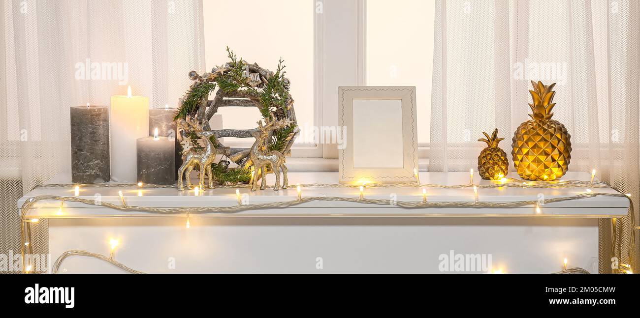 Christmas wreath with glowing lights and candles on mantelpiece near