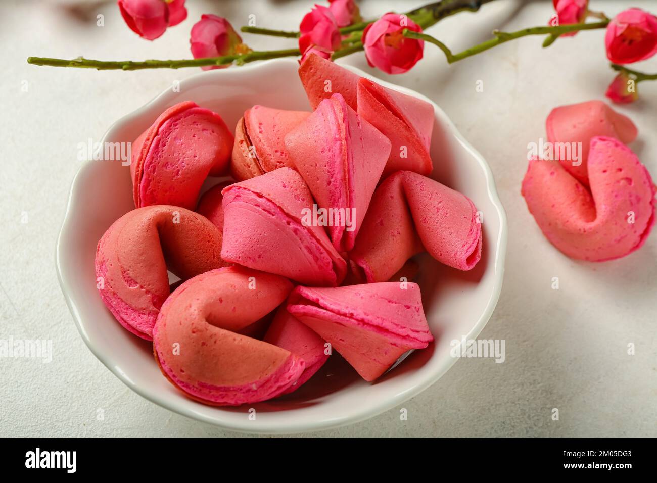 Bowl of pink fortune cookies and sakura on white background, closeup