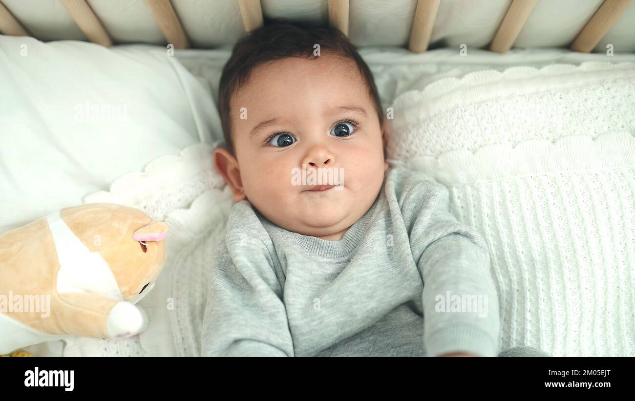 Adorable hispanic baby lying on bed with relaxed expression at bedroom