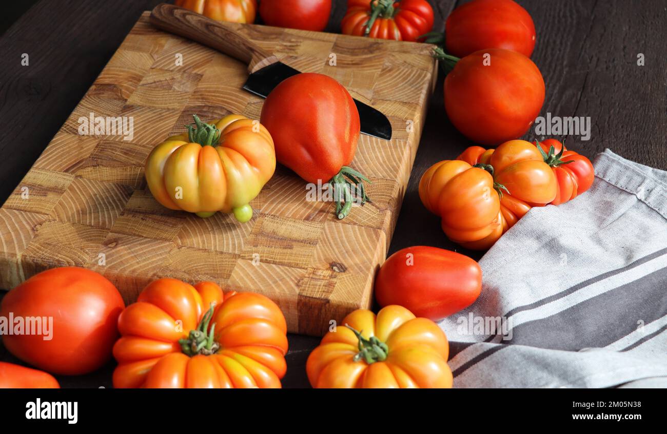 Fresh ripe hairloom tomatoes and knife on rustic wooden board over dark background . Stock Photo